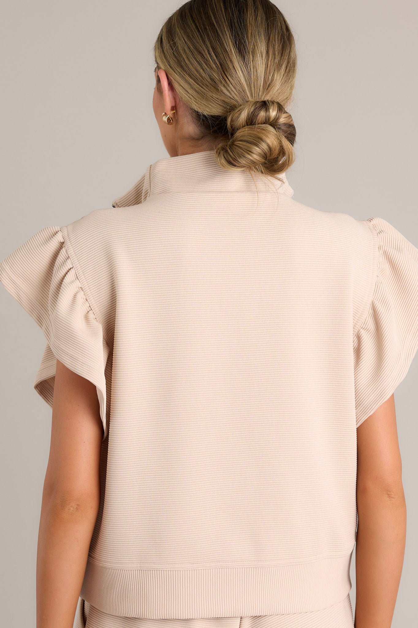 Back view of a tan top showcasing the ribbed fabric, wide ruffled sleeves, and thick hemline.