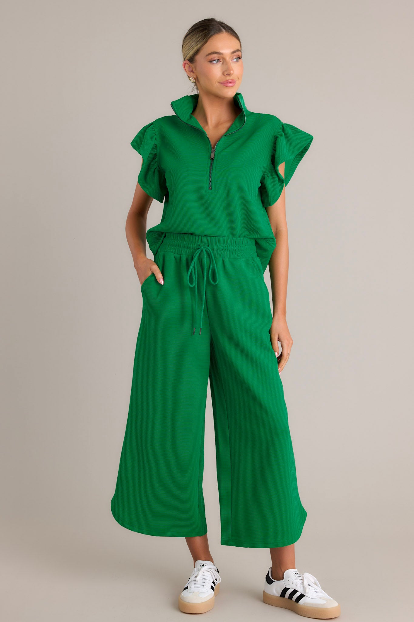 Full length view of a green top with a functional zip up neckline, ribbed fabric, wide ruffled sleeves, and a thick hemline