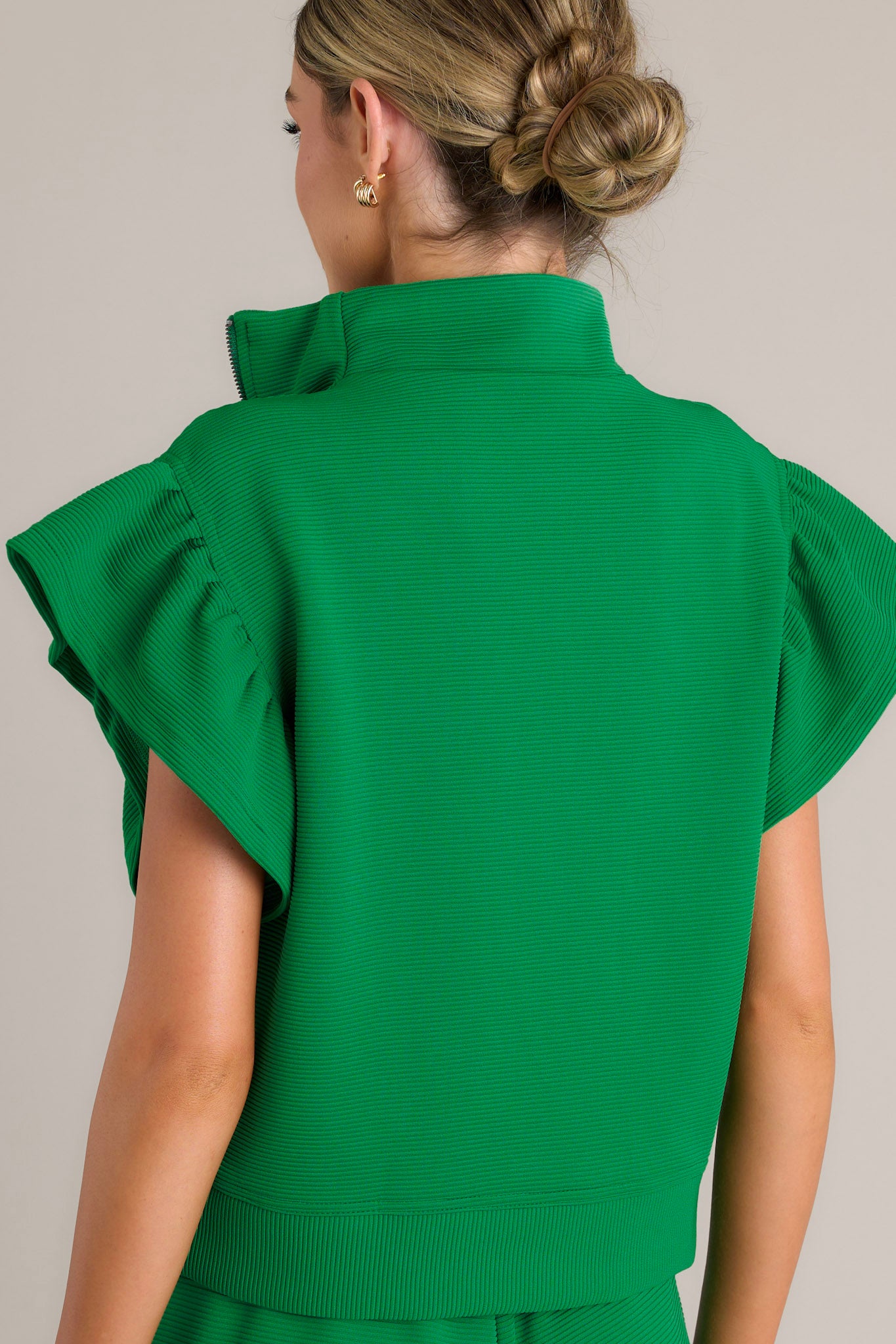 Back view of a green top highlighting the ribbed fabric and the wide ruffled sleeves.