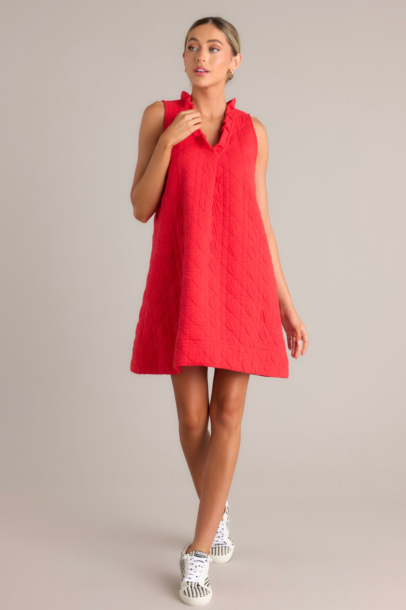 Action shot of a red mini dress displaying the flow and movement of the fabric, highlighting the ruffled v-neckline, unique quilted material, functional hip pockets, and sleeveless design.