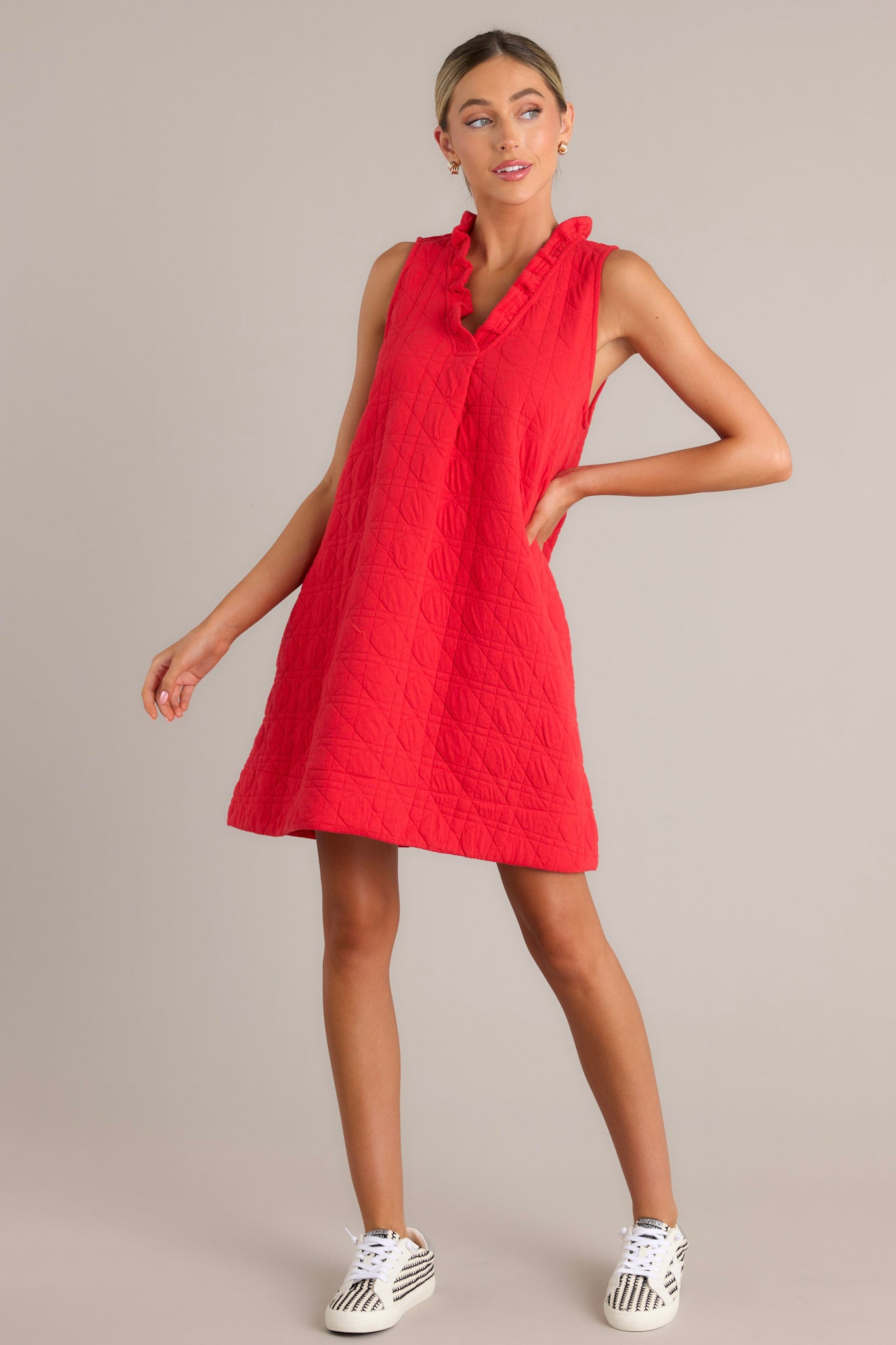 Full length view of a red mini dress with a ruffled v-neckline, unique quilted material, functional hip pockets, and a sleeveless design.