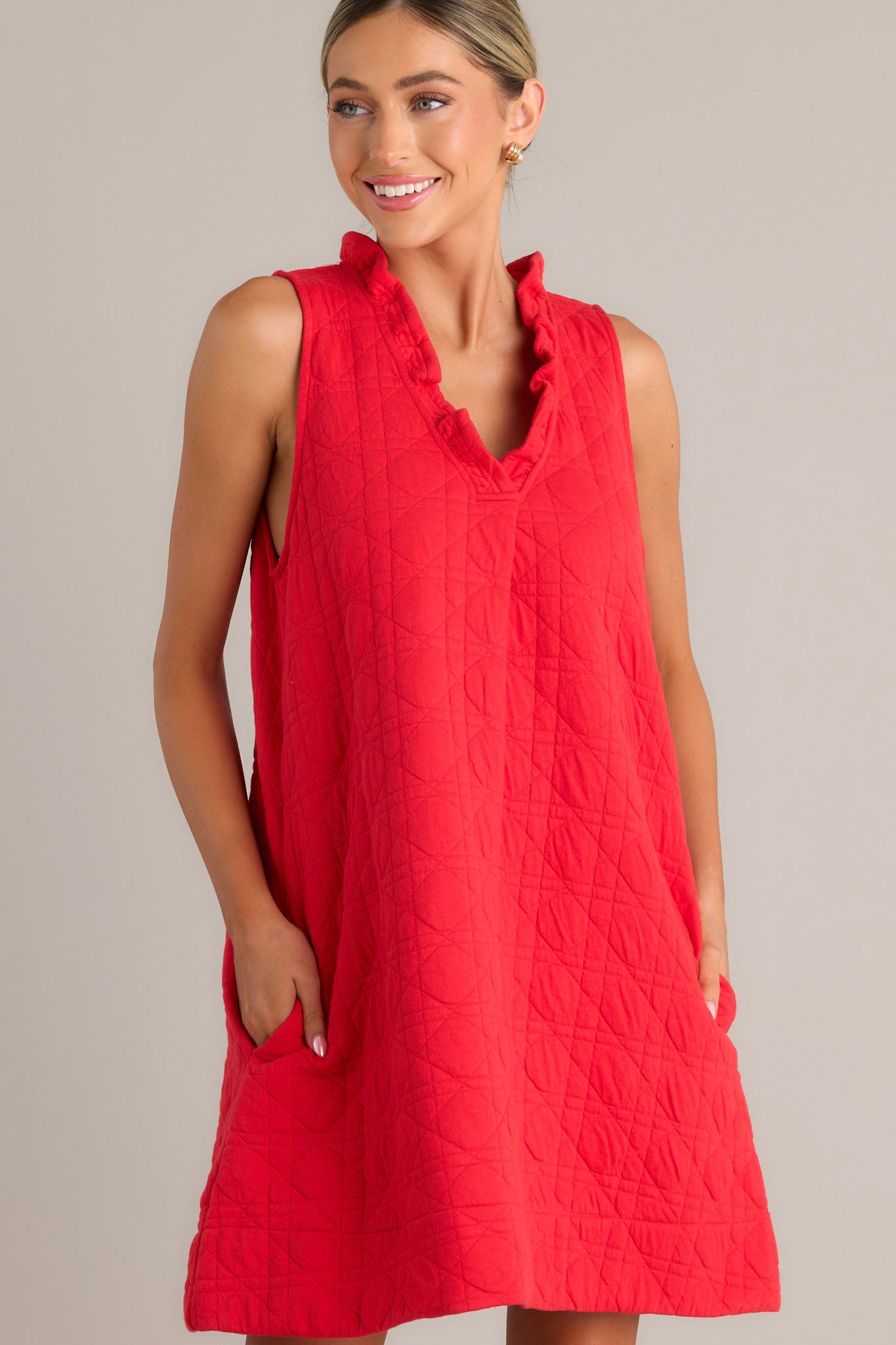 This red mini dress features a ruffled v-neckline, a unique quilted material, functional hip pockets, and a sleeveless design.