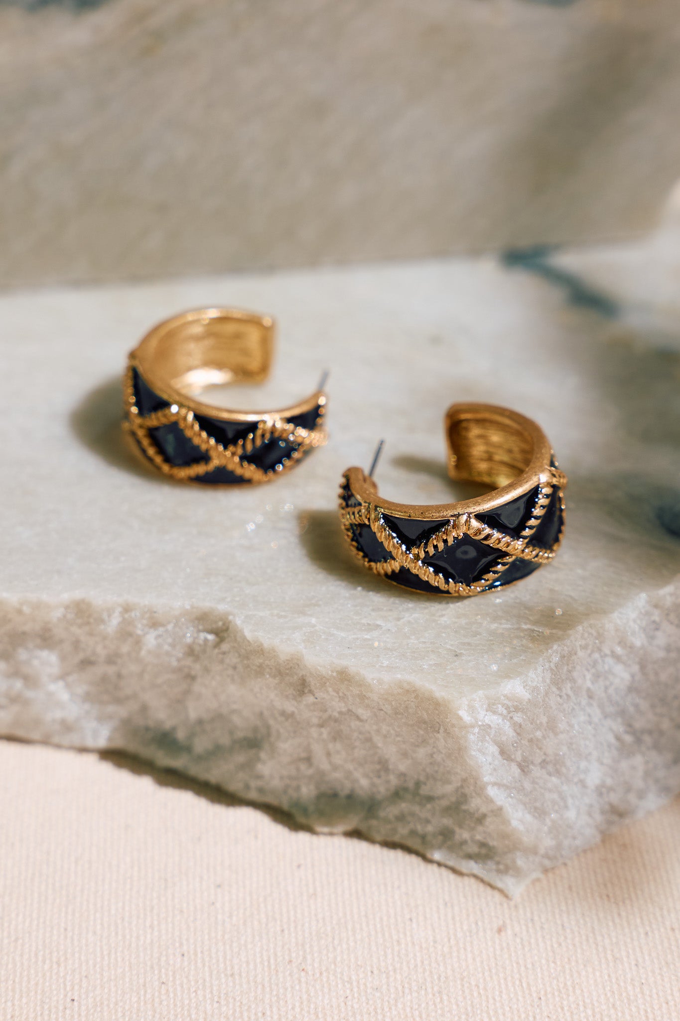 Black open hoop earrings with a gold trim and criss cross pattern along the hoop. 