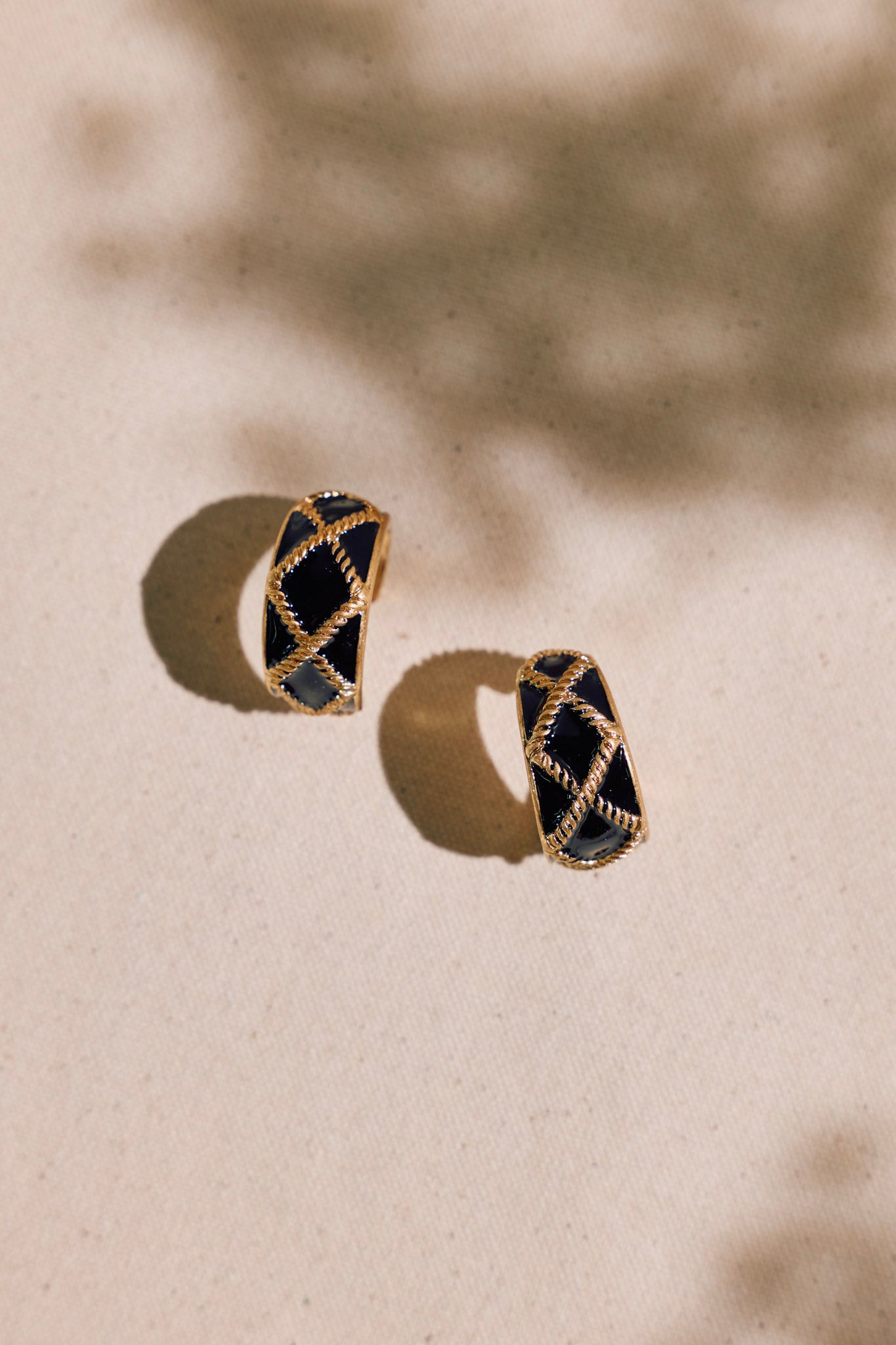 Detailed view of these black earrings that feature an incomplete hoop design, a gold textured design, and secure post backings.