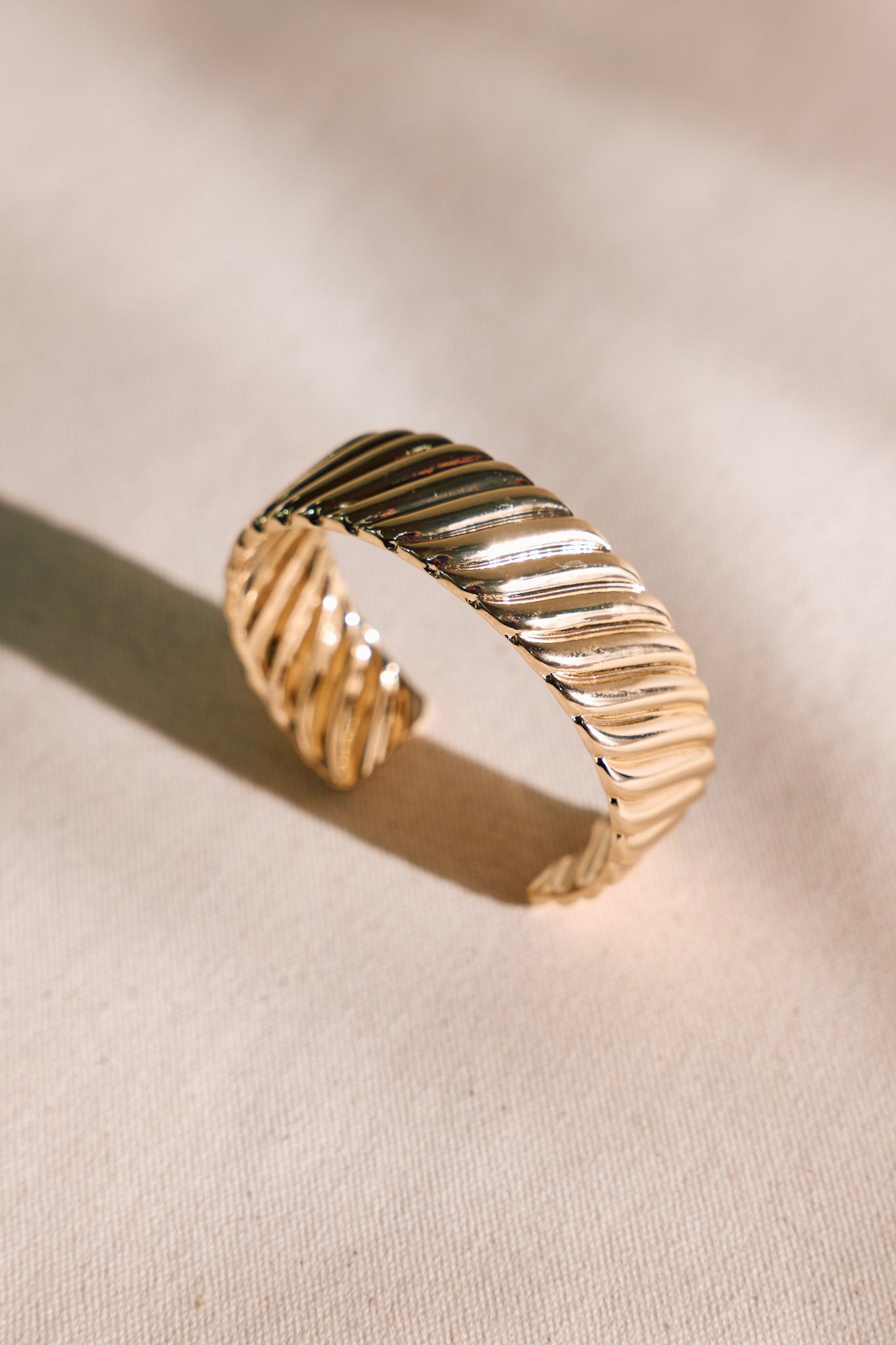 Overhead view of this gold cuff bracelet that features gold hardware, a ripple textured design, and a open structure design.