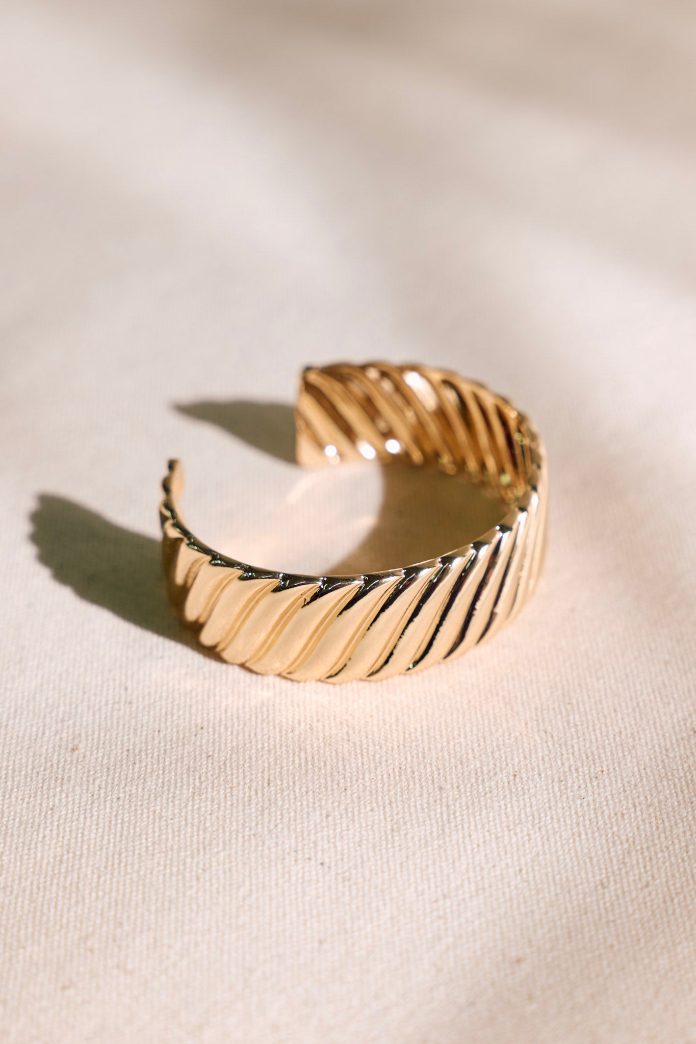 Side view of this gold cuff bracelet that features gold hardware, a ripple textured design, and a open structure design.