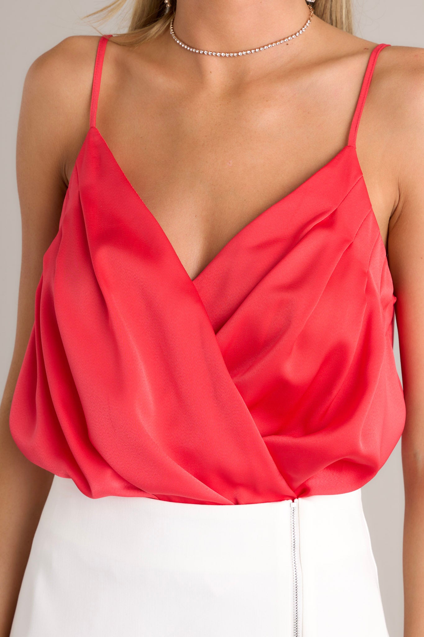 Close-up of the red bodysuit showing the v-neckline with a snap button feature, gathering in the chest area, and the thin adjustable straps.