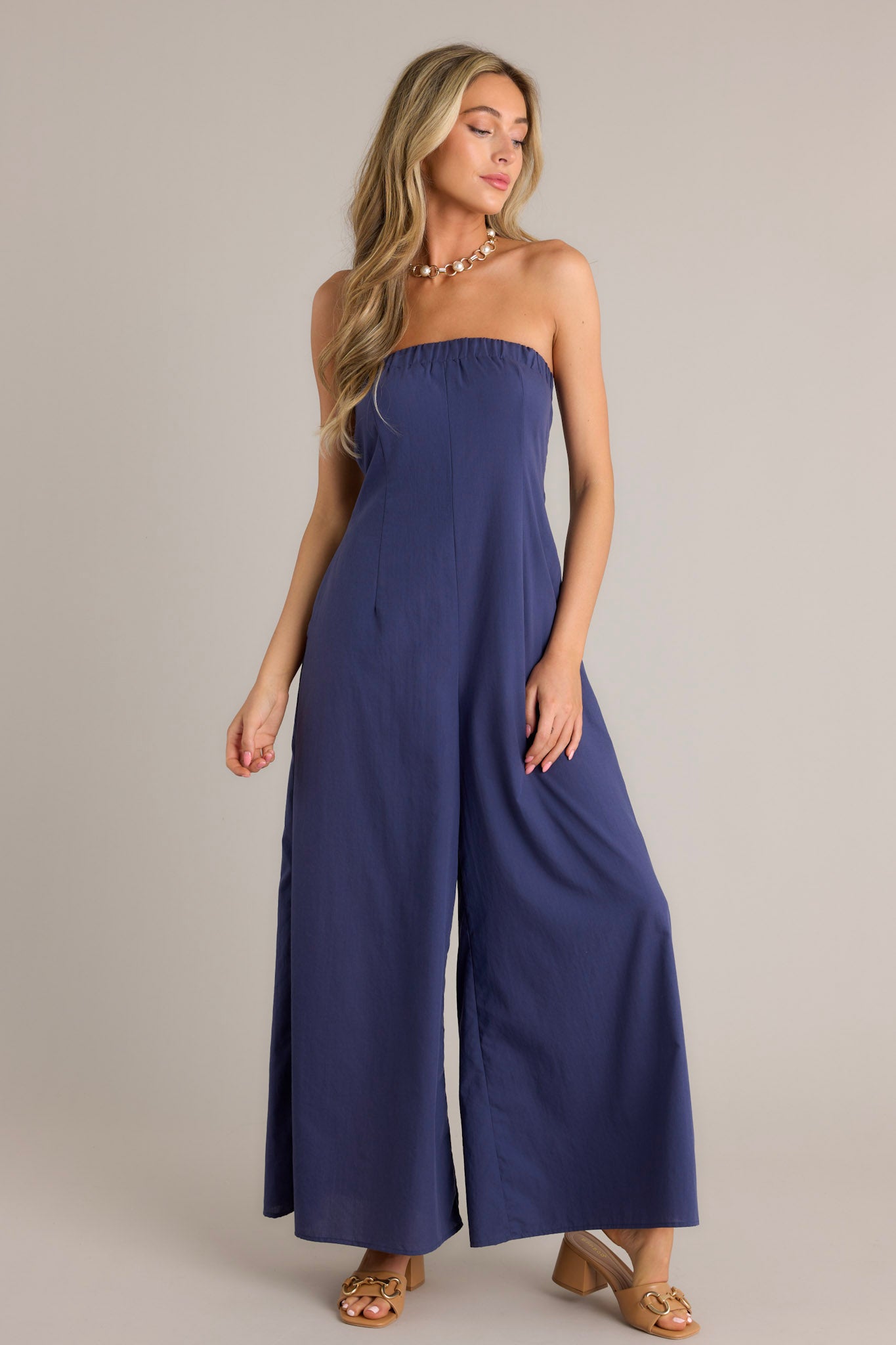 Action shot of a navy jumpsuit displaying the flow and movement, highlighting the elastic strapless neckline, elastic cut-out in the back, functional hip pockets, and wide leg design.