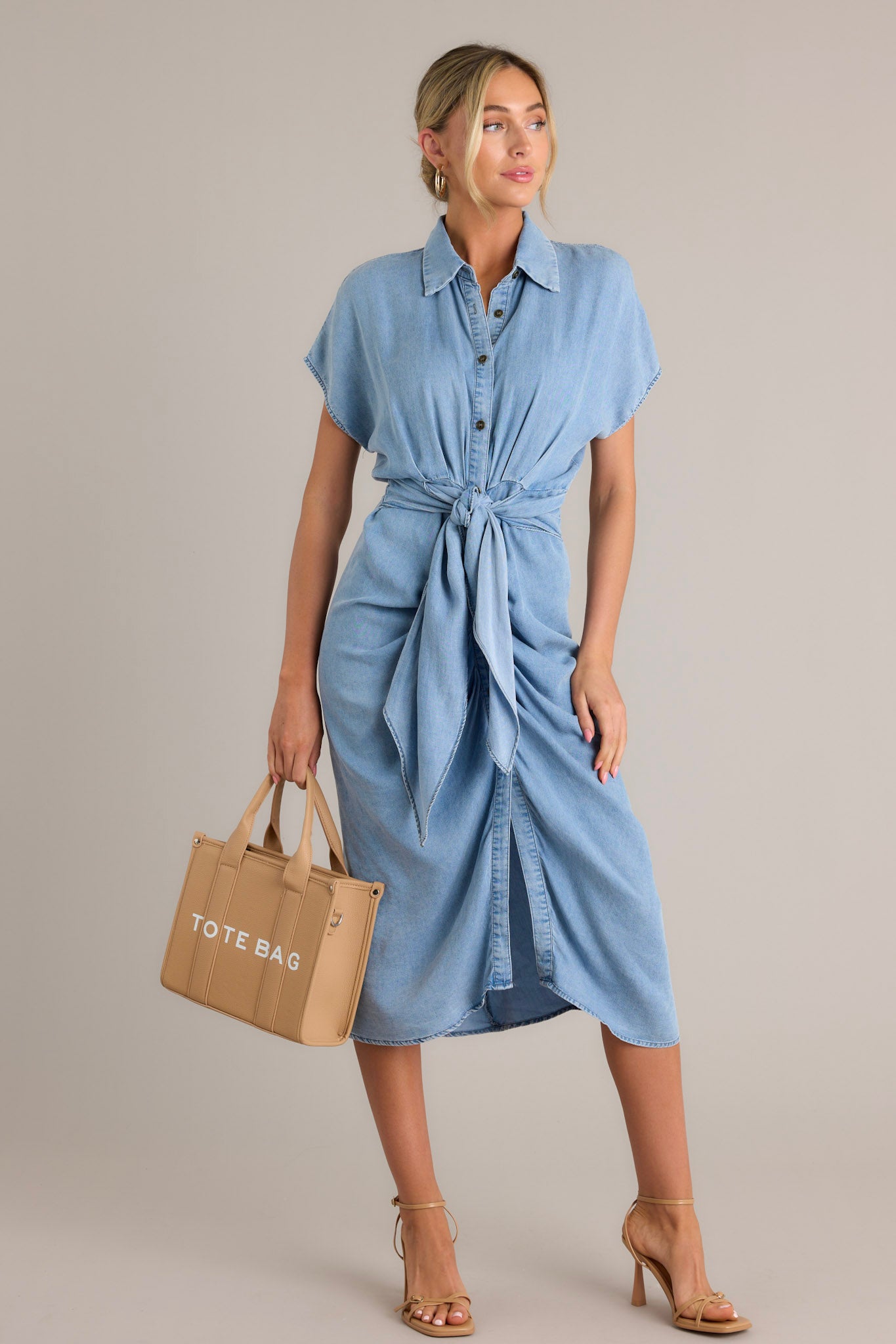 This blue dress features a collared neckline, a full button front, a self-tie waist feature, a front slit, and short sleeves.