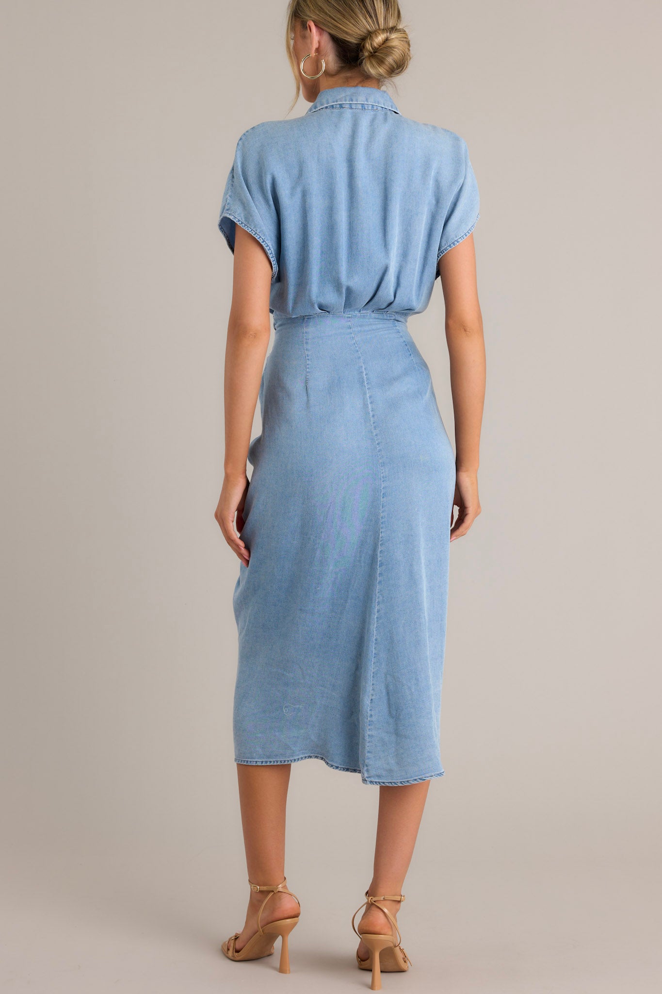 Back view of this dress that features a collared neckline, a full button front, a self-tie waist feature, a front slit, and short sleeves.