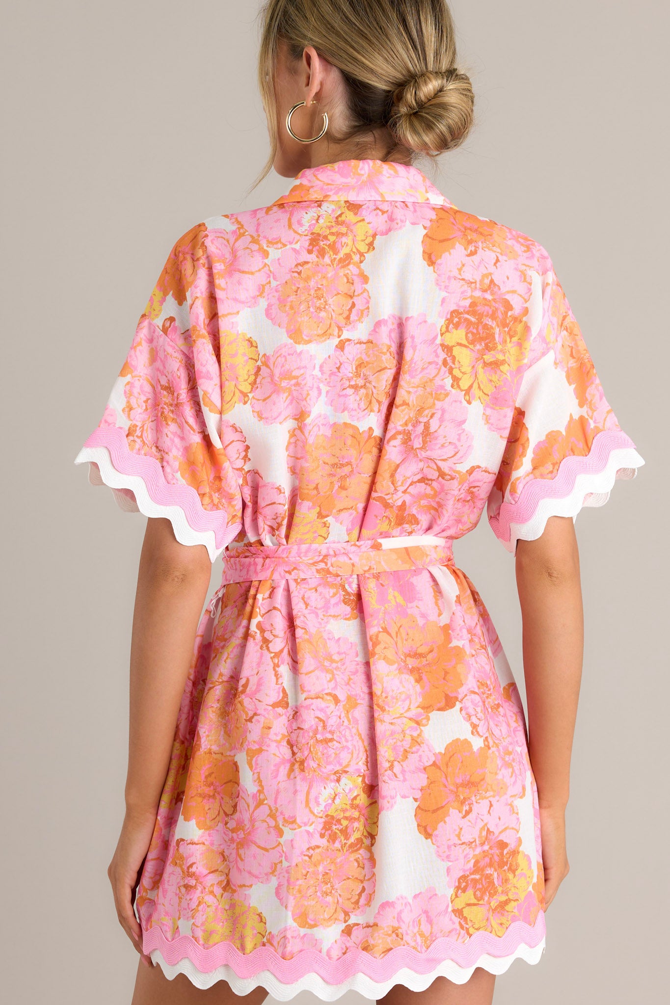 Back view of a light pink floral mini dress highlighting the collared neckline, self-tie waist belt, ricrac trim throughout, and overall fit.