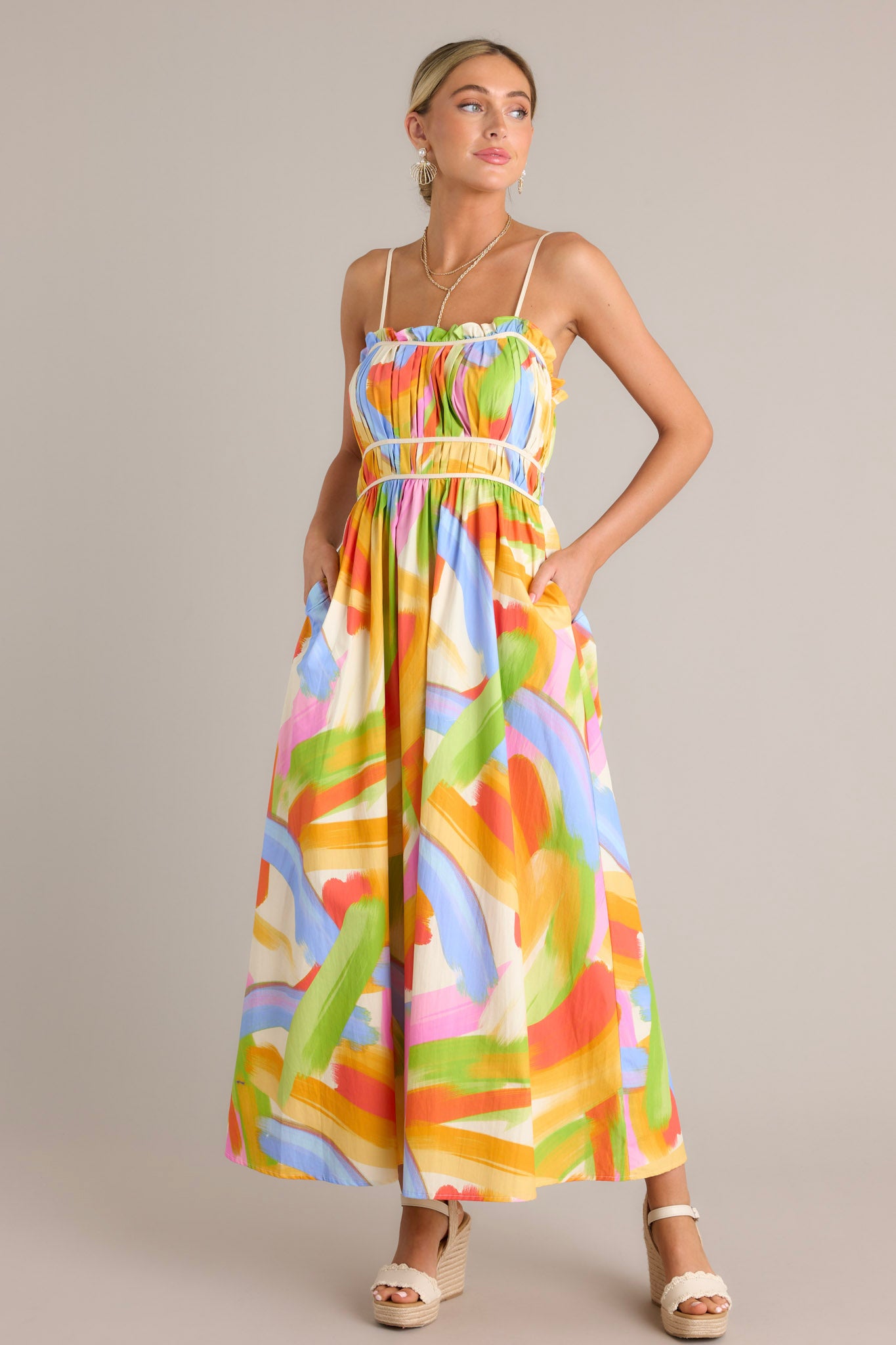 This yellow multi maxi dress features a square neckline, thin adjustable straps, a pleated chest, elastic waist inserts, functional hip pockets, and a flowing silhouette.