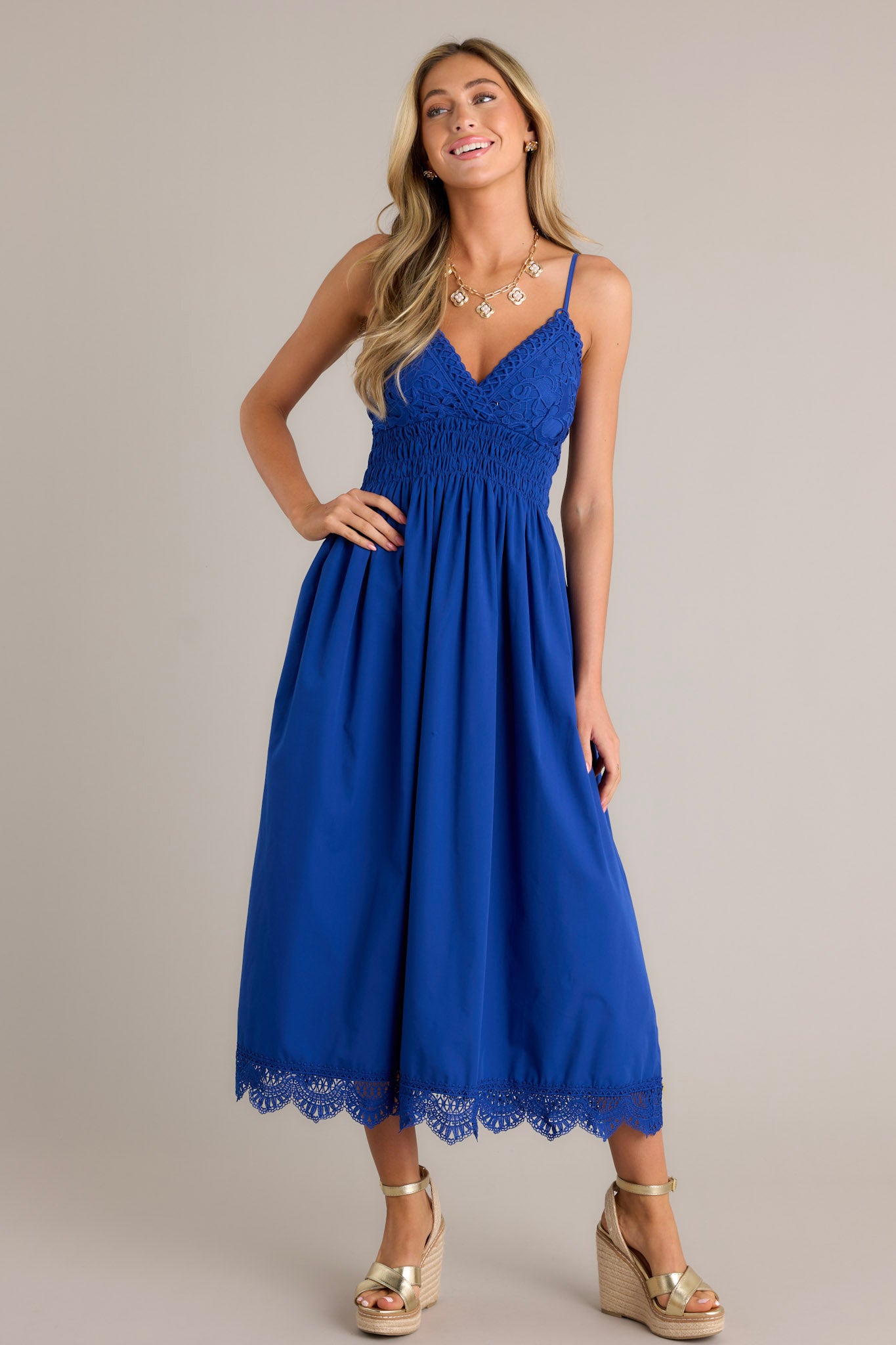 Front angled view of a blue maxi dress featuring a v-neckline, thin adjustable straps, a lace bust, a fully smocked waist & back, a flowing silhouette, and a lace hemline