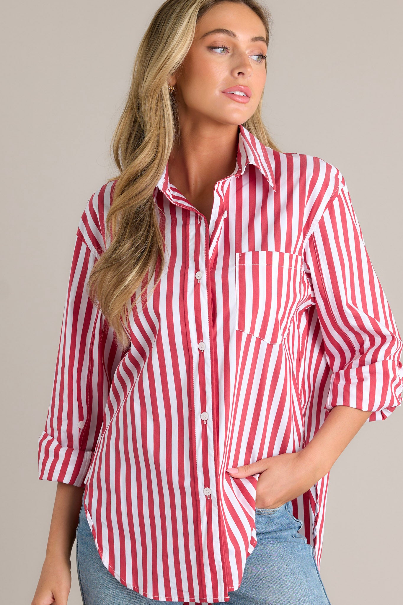 Side view of a red stripe top showcasing the collared neckline, functional button front, breast pocket, rollable button cuffed sleeves, and split high-low hemline.