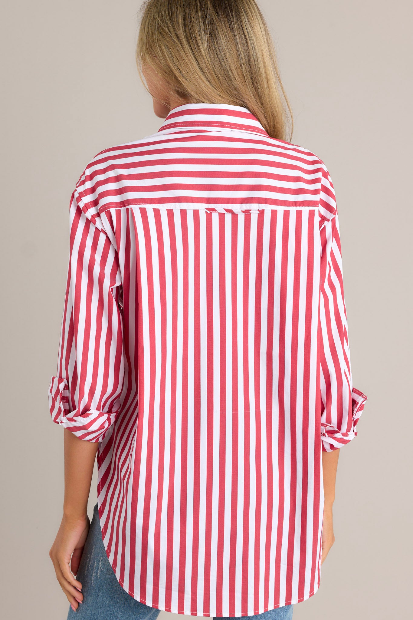 Back view of a red stripe top highlighting the rollable button cuffed sleeves and split high-low hemline.