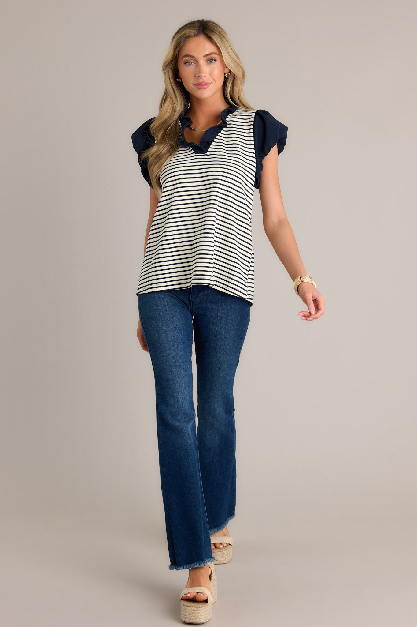 Full length view of a beige stripe blouse with a navy ruffle v-neckline, navy and beige horizontal stripes, and slightly cuffed short sleeves