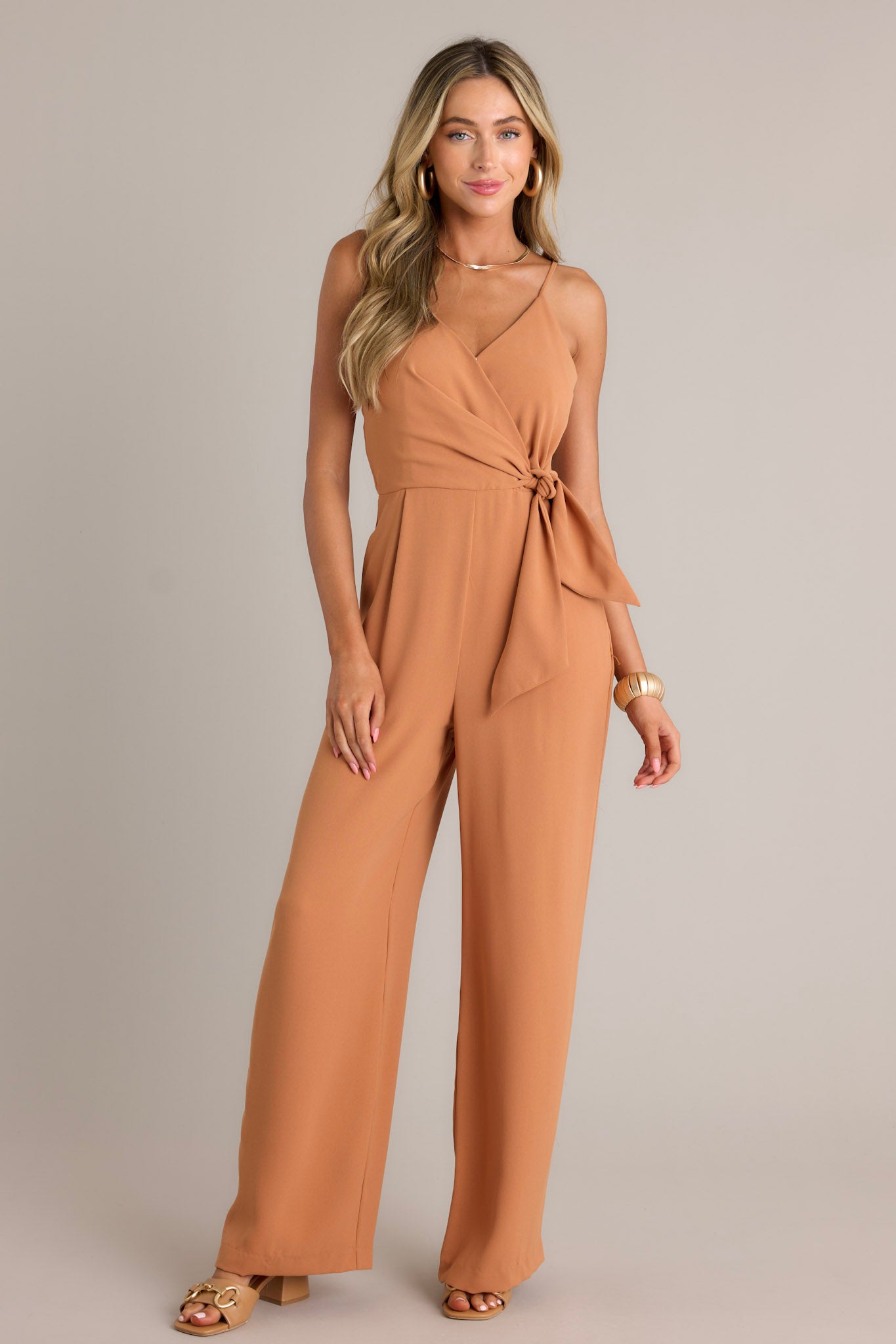 Full length view of a jumpsuit with a v-neckline, thin adjustable straps, an elastic waist insert, a self-tie waist feature, a discrete side zipper, functional hip pockets, and a wide leg design