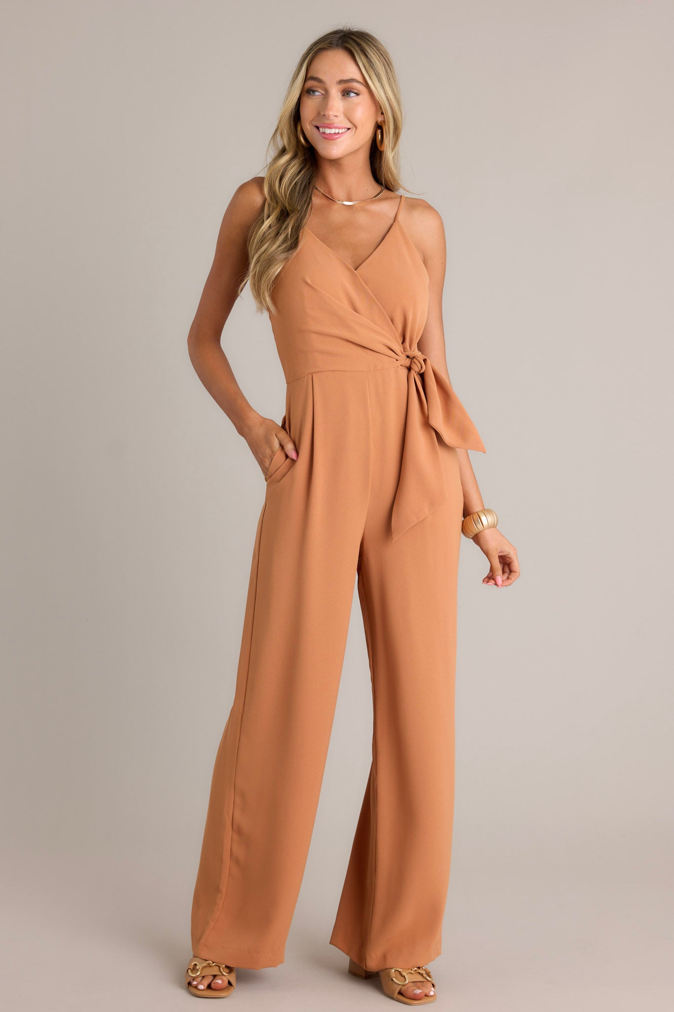 Action shot of a jumpsuit displaying the fit and movement, highlighting the v-neckline, thin adjustable straps, elastic waist insert, self-tie waist feature, functional hip pockets, and wide leg design.