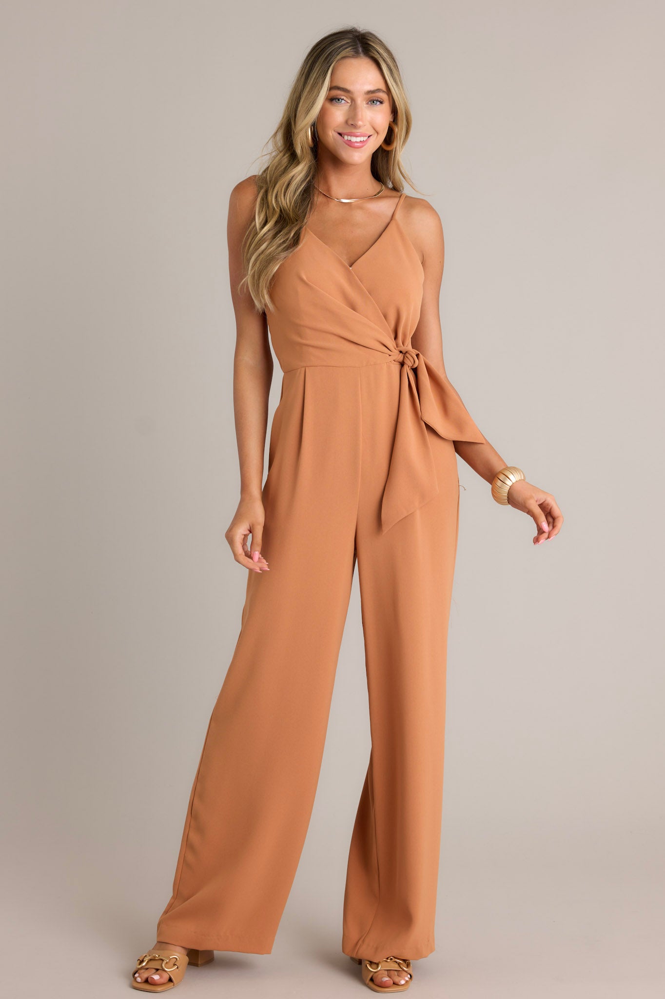 Front view of a jumpsuit featuring a v-neckline, thin adjustable straps, an elastic waist insert, a self-tie waist feature, a discrete side zipper, functional hip pockets, and a wide leg design.