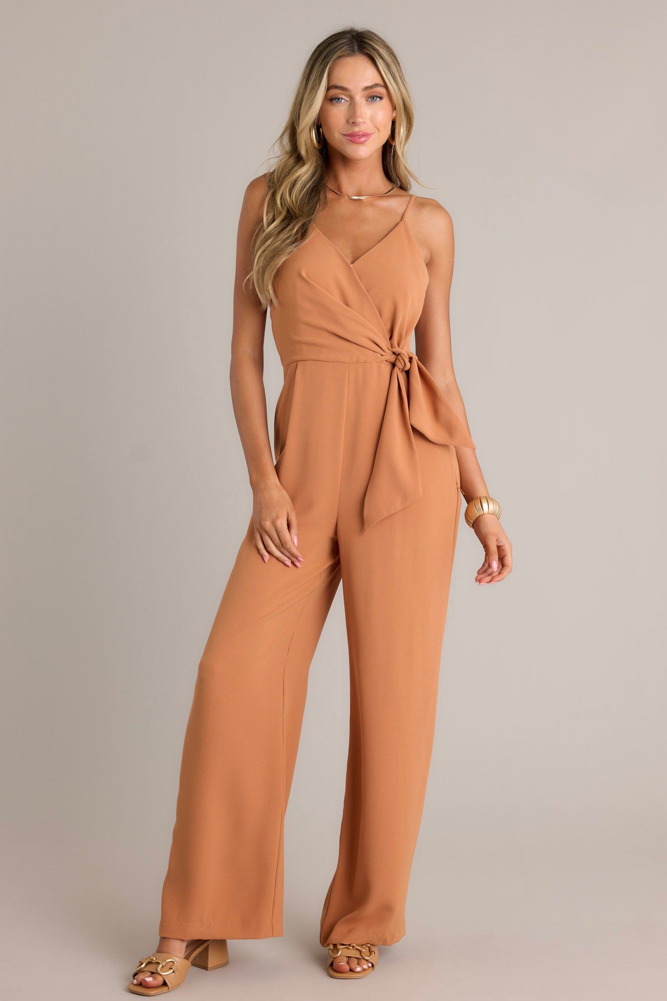 Action shot of a jumpsuit displaying the fit and movement, highlighting the v-neckline, thin adjustable straps, elastic waist insert, self-tie waist feature, functional hip pockets, and wide leg design.