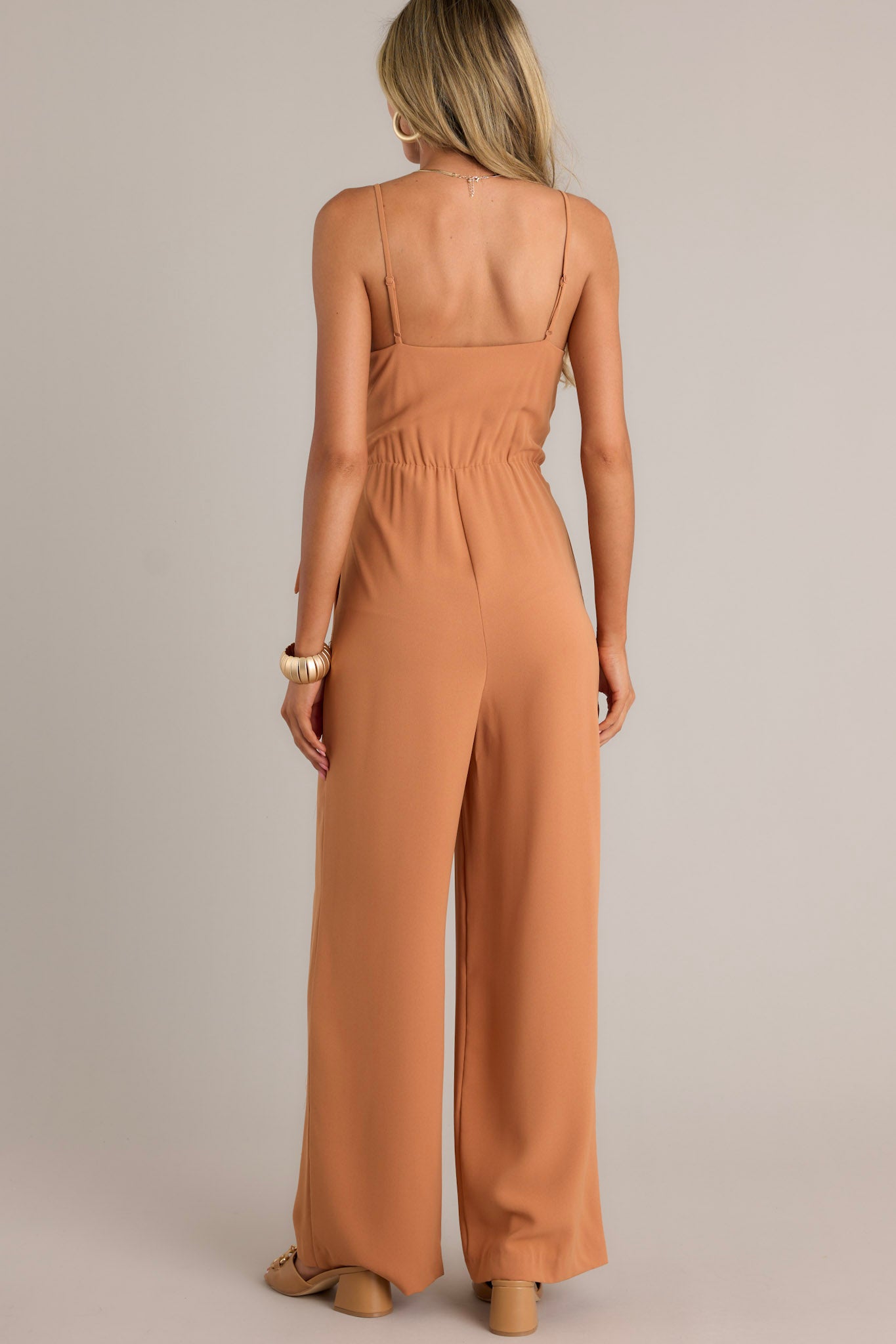 Back view of a jumpsuit highlighting the thin adjustable straps, elastic waist insert, and overall fit.