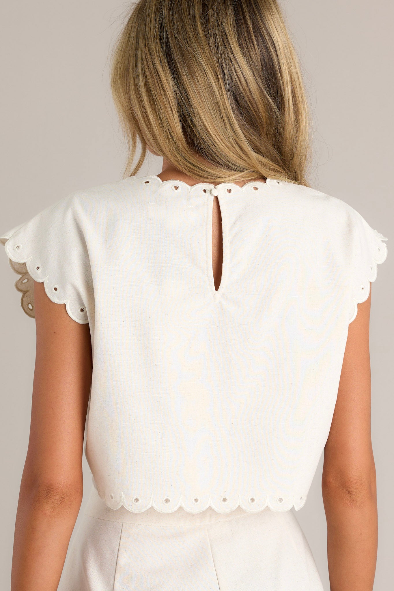 Back view of an ivory top highlighting the scalloped neckline, wide scalloped short sleeves, and overall fit.