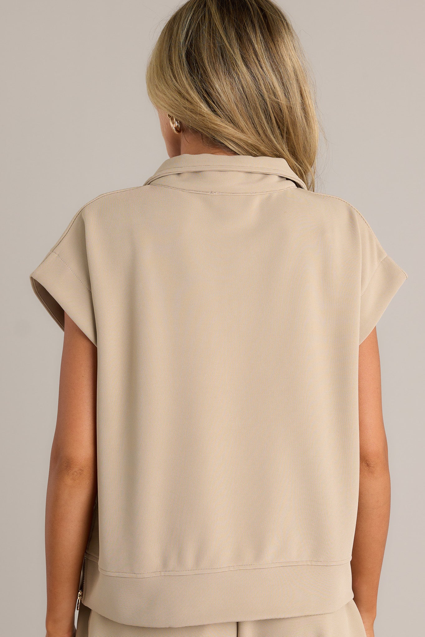 Back view of a tan pullover highlighting the overall fit, short cap sleeves, and functional zippers on the sides.