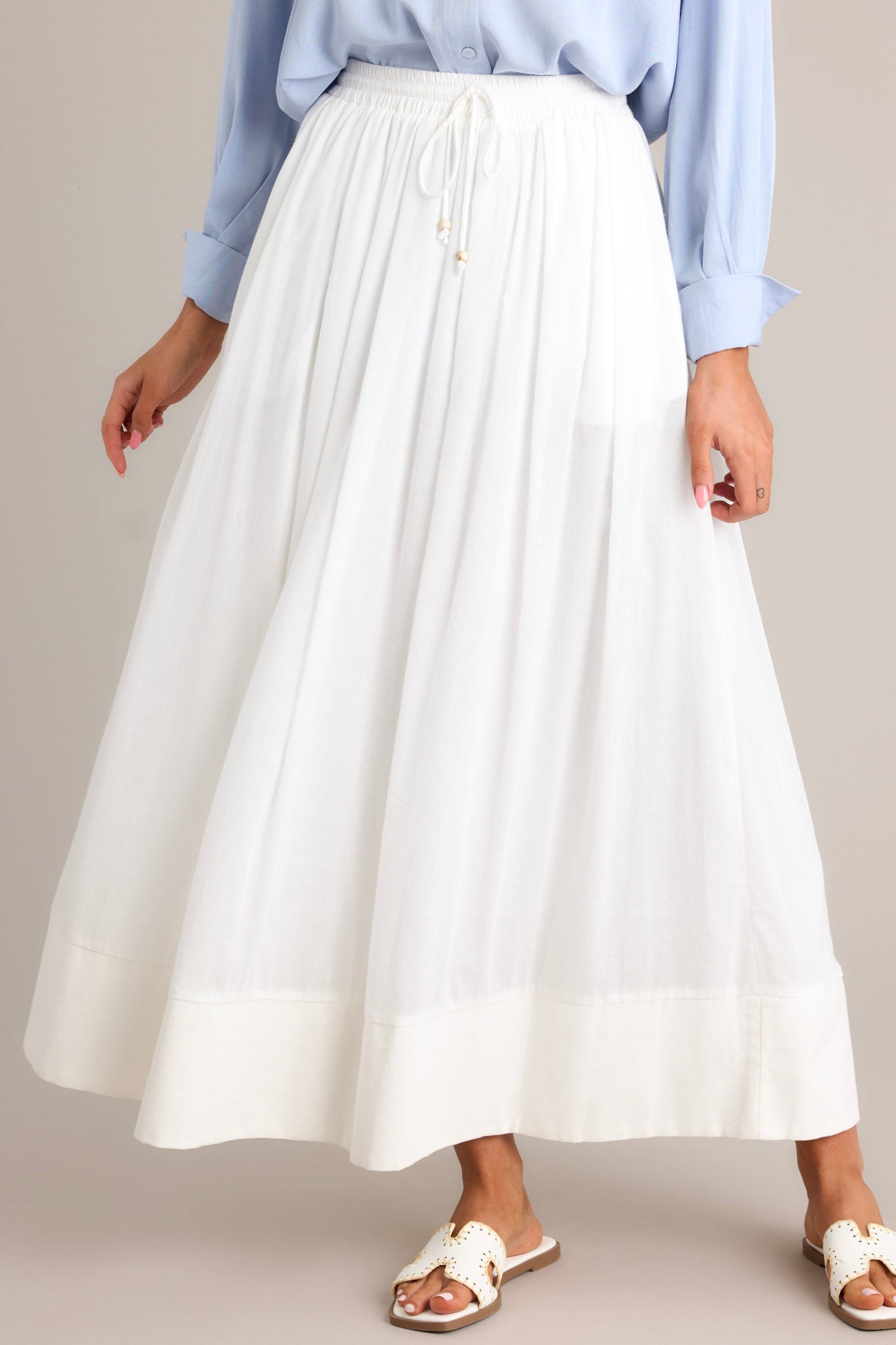 Front view of this skirt that features a high waisted design, an elastic waistband, a self-tie drawstring, functional pockets, flowing fabric, and a thick hemline.