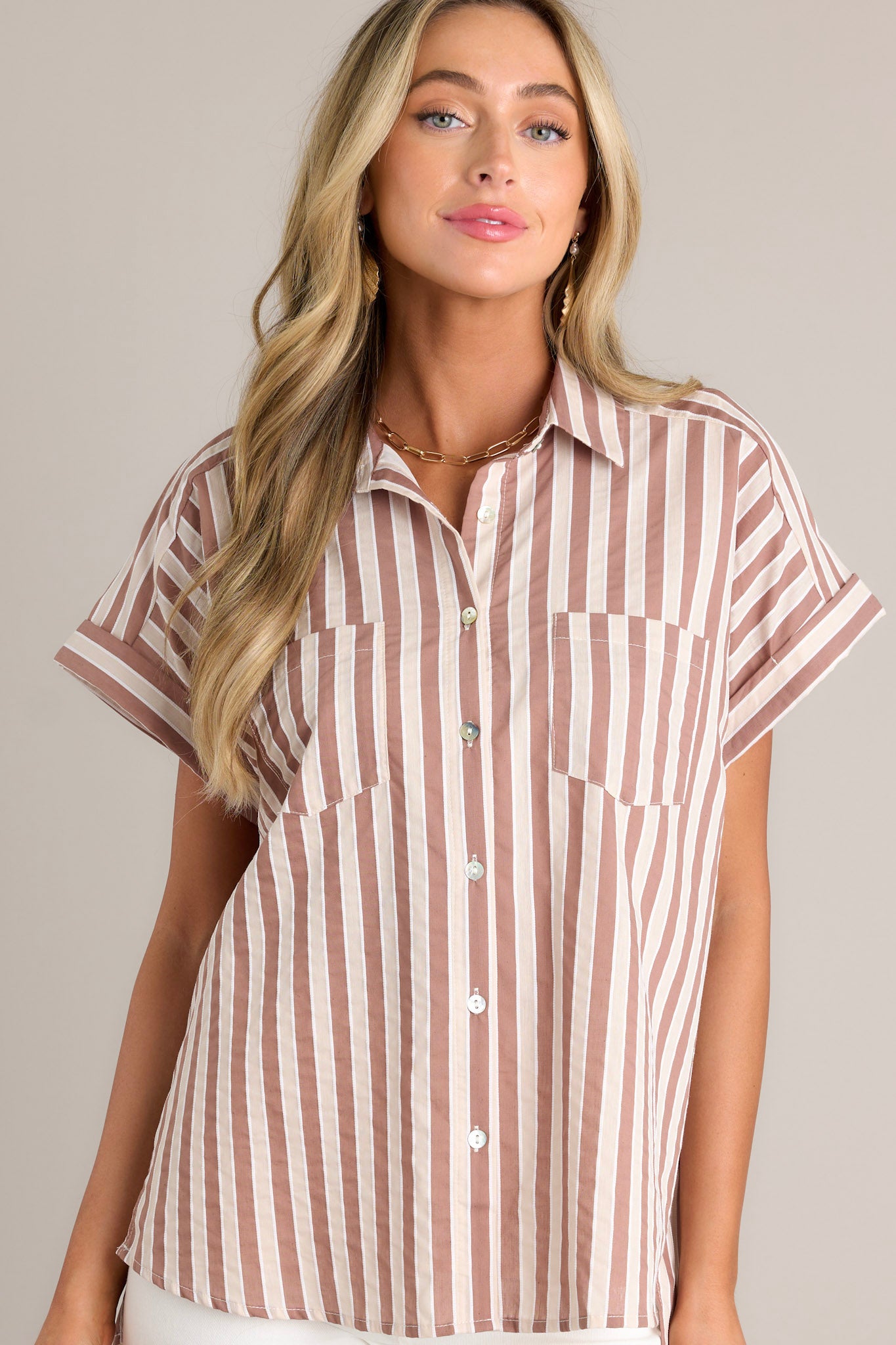 Front view of a tan stripe top featuring a collared neckline, a full button front, functional breast pockets, a vertical stripe design, cuffed short sleeves, and a split scooped hemline.