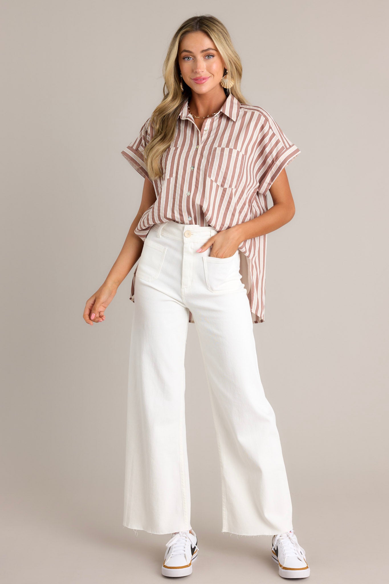 Full length view of a tan stripe top with a collared neckline, a full button front, functional breast pockets, a vertical stripe design, cuffed short sleeves, and a split scooped hemline