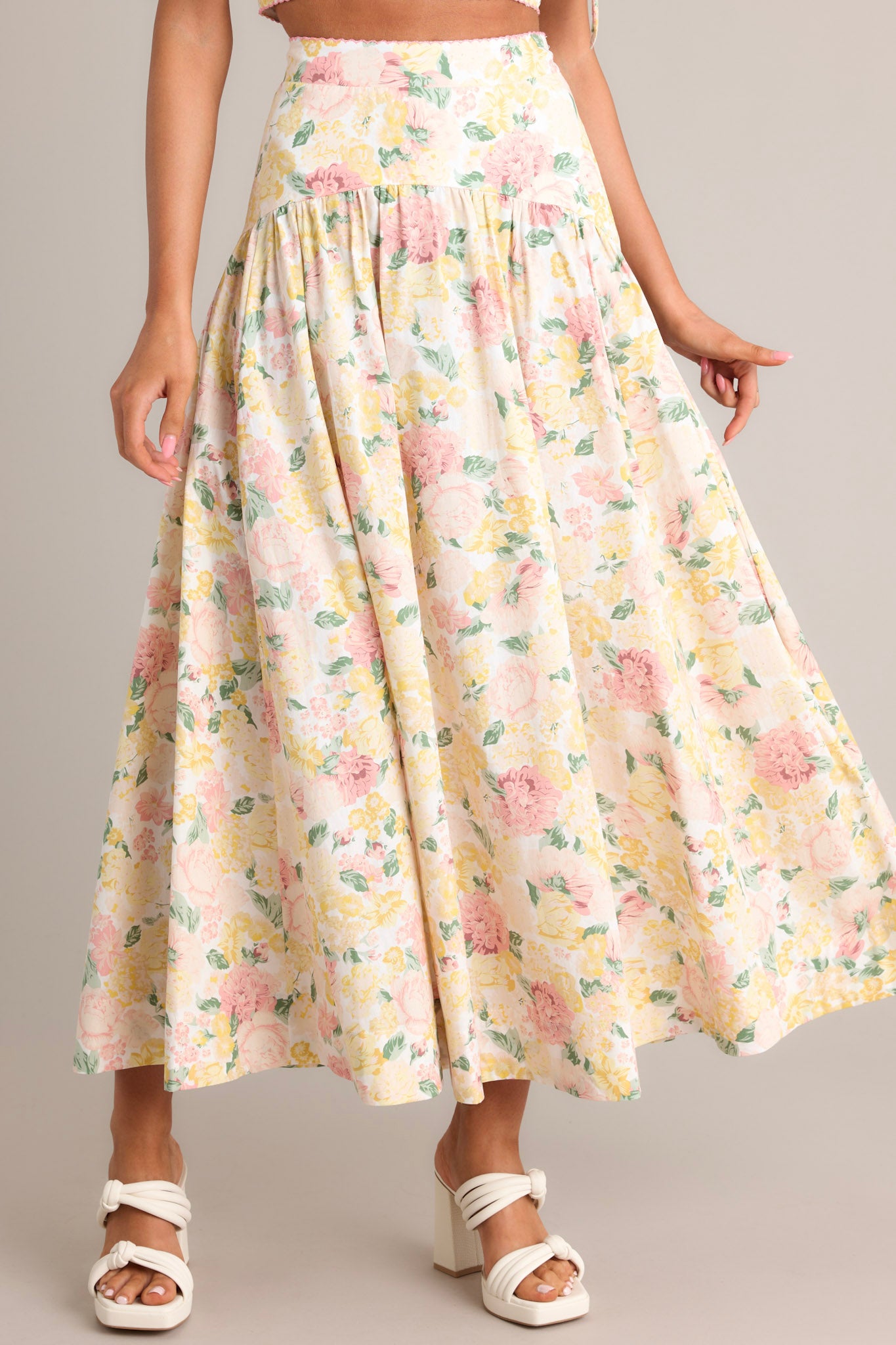 Front view of an ivory floral maxi skirt featuring a scalloped high waisted design, an elastic waist insert, a discrete side zipper, gathering around the hips, and a flowing silhouette.