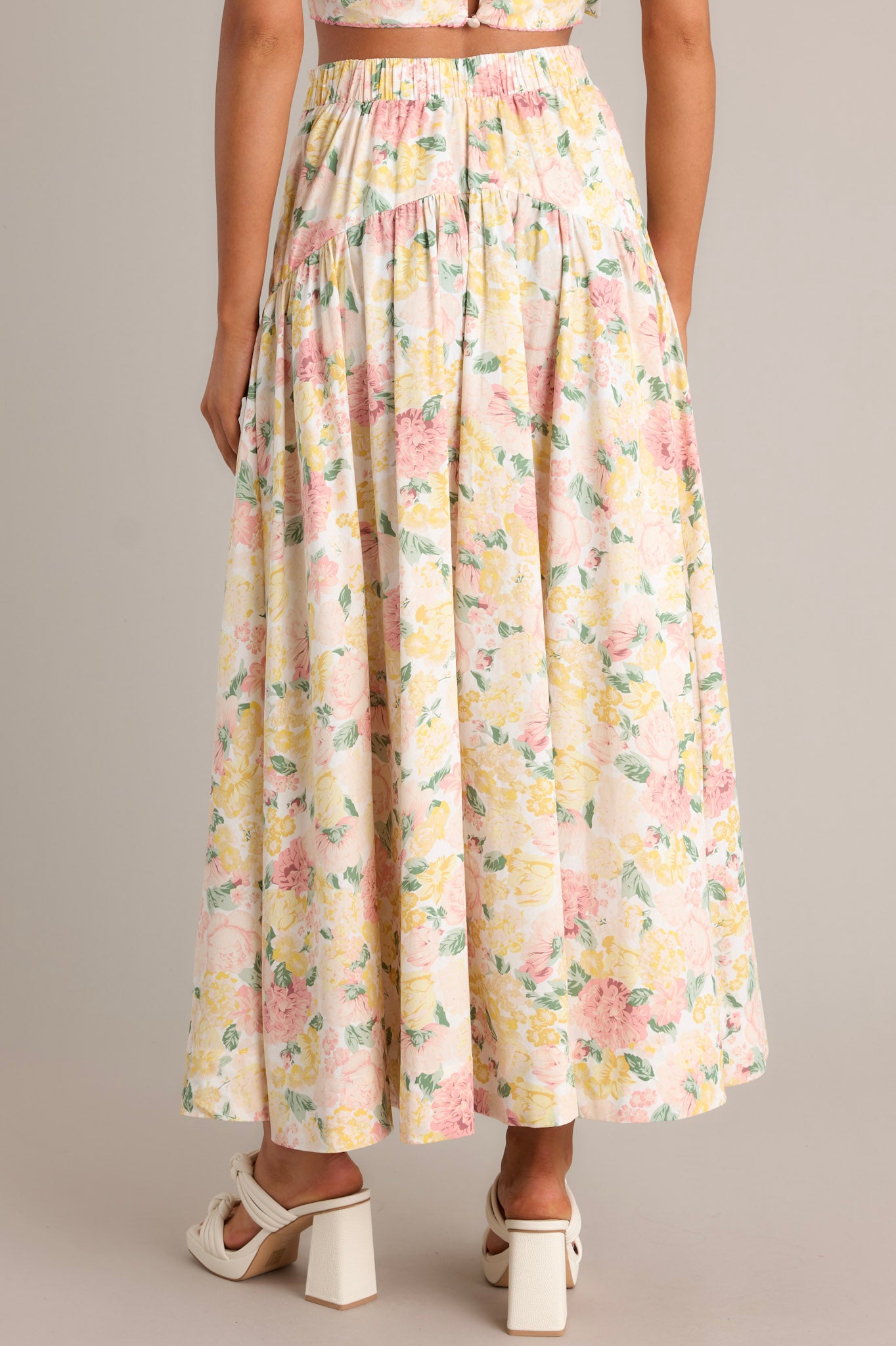 Back view of an ivory floral maxi skirt highlighting the elastic waist insert, scalloped high waisted design, and overall fit.