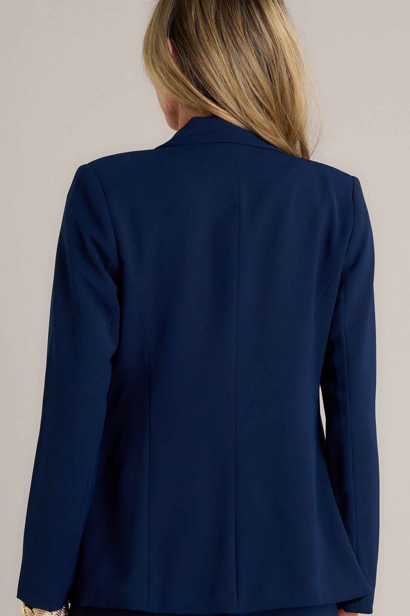 Back view of a navy blazer highlighting the shoulder padding, long sleeves, and overall fit.