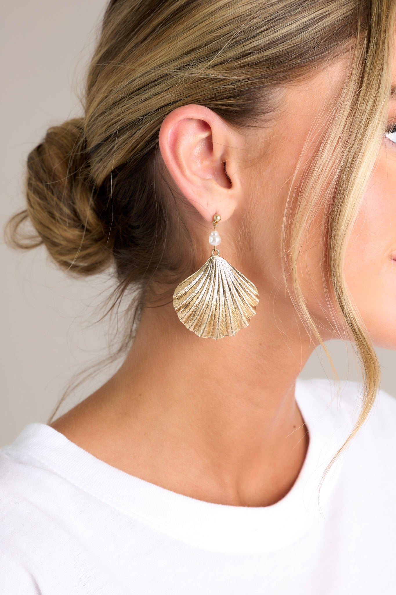 These gold earrings feature a gold seashell pendant and a small faux pearl detail.