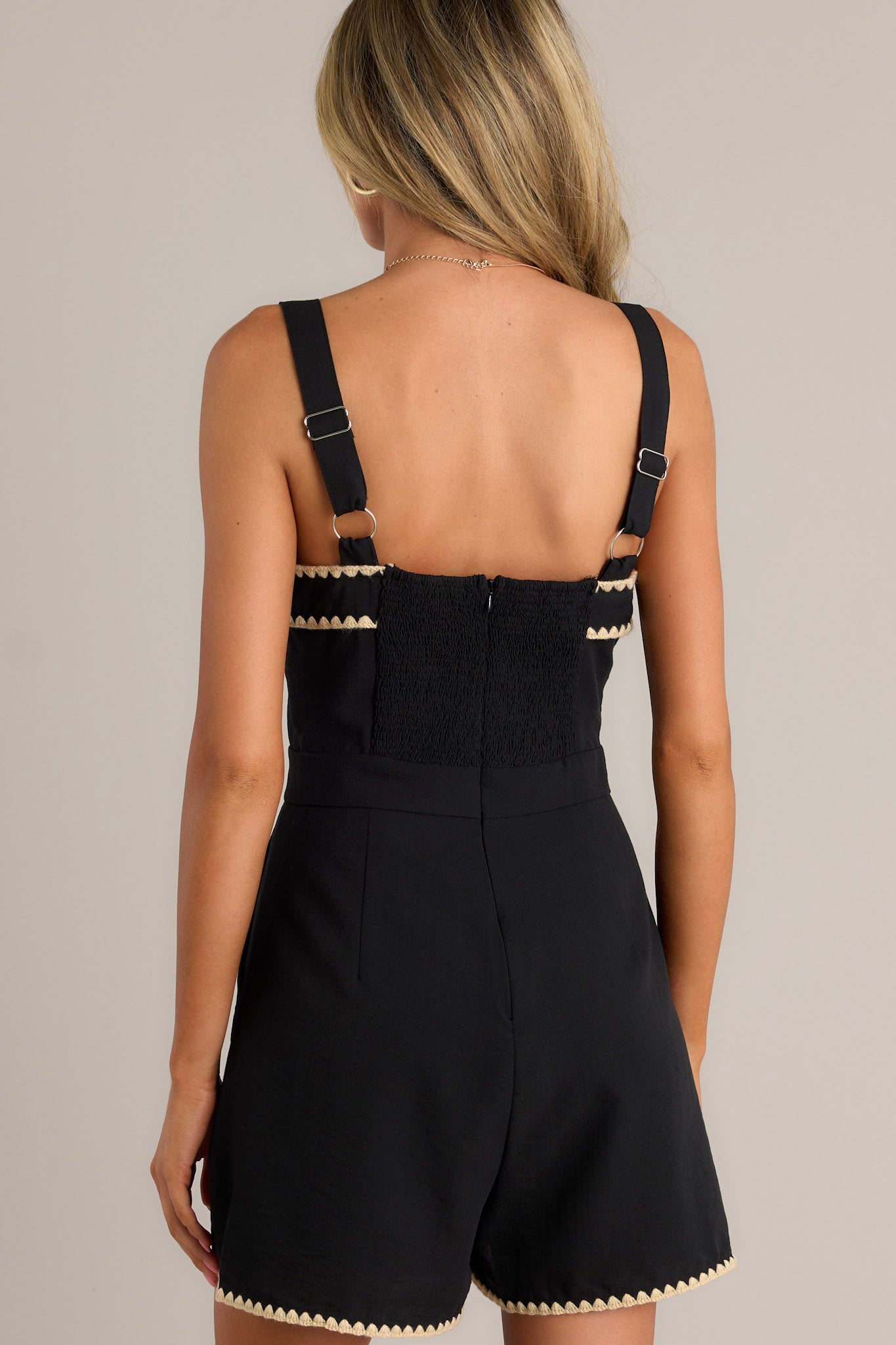 Back view of a black romper highlighting the smocked back insert, discrete zipper, and overall fit.