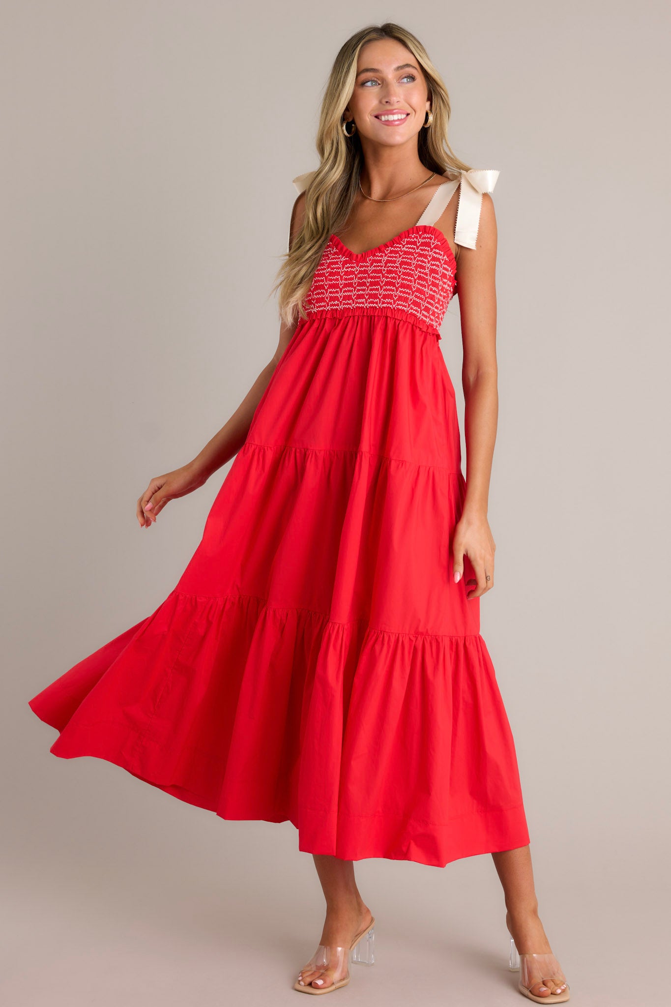 This red maxi dress features a v-neckline, thick self-tie straps, a fully smocked bodice, functional hip pockets, and a tiered design.