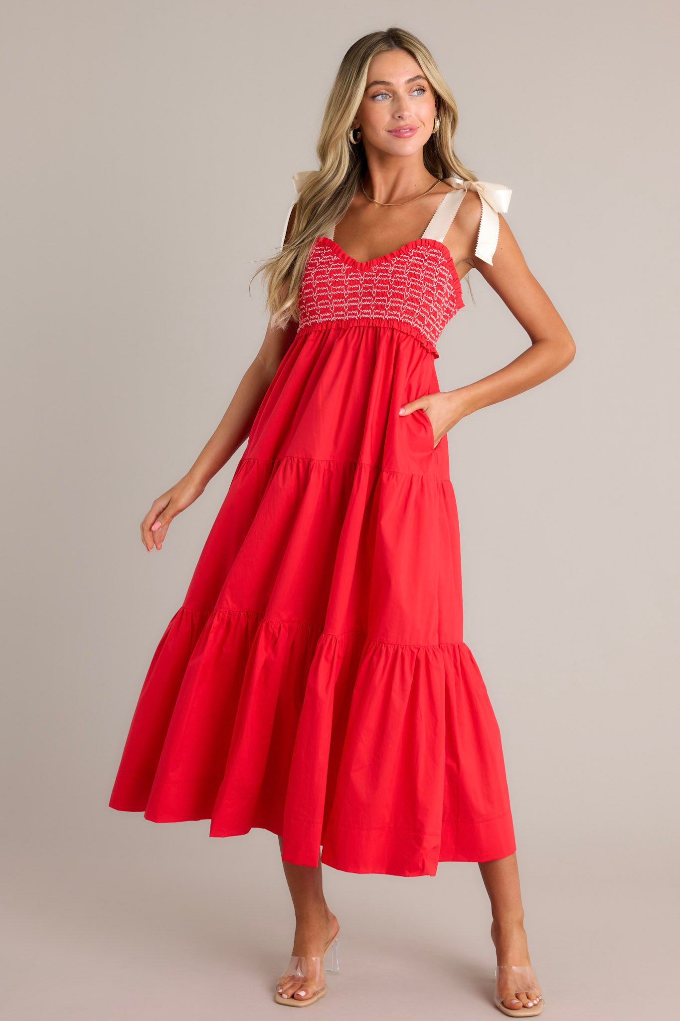 Action shot of a red maxi dress displaying the fit and movement, highlighting the v-neckline, thick self-tie straps, fully smocked bodice, functional hip pockets, and tiered design.