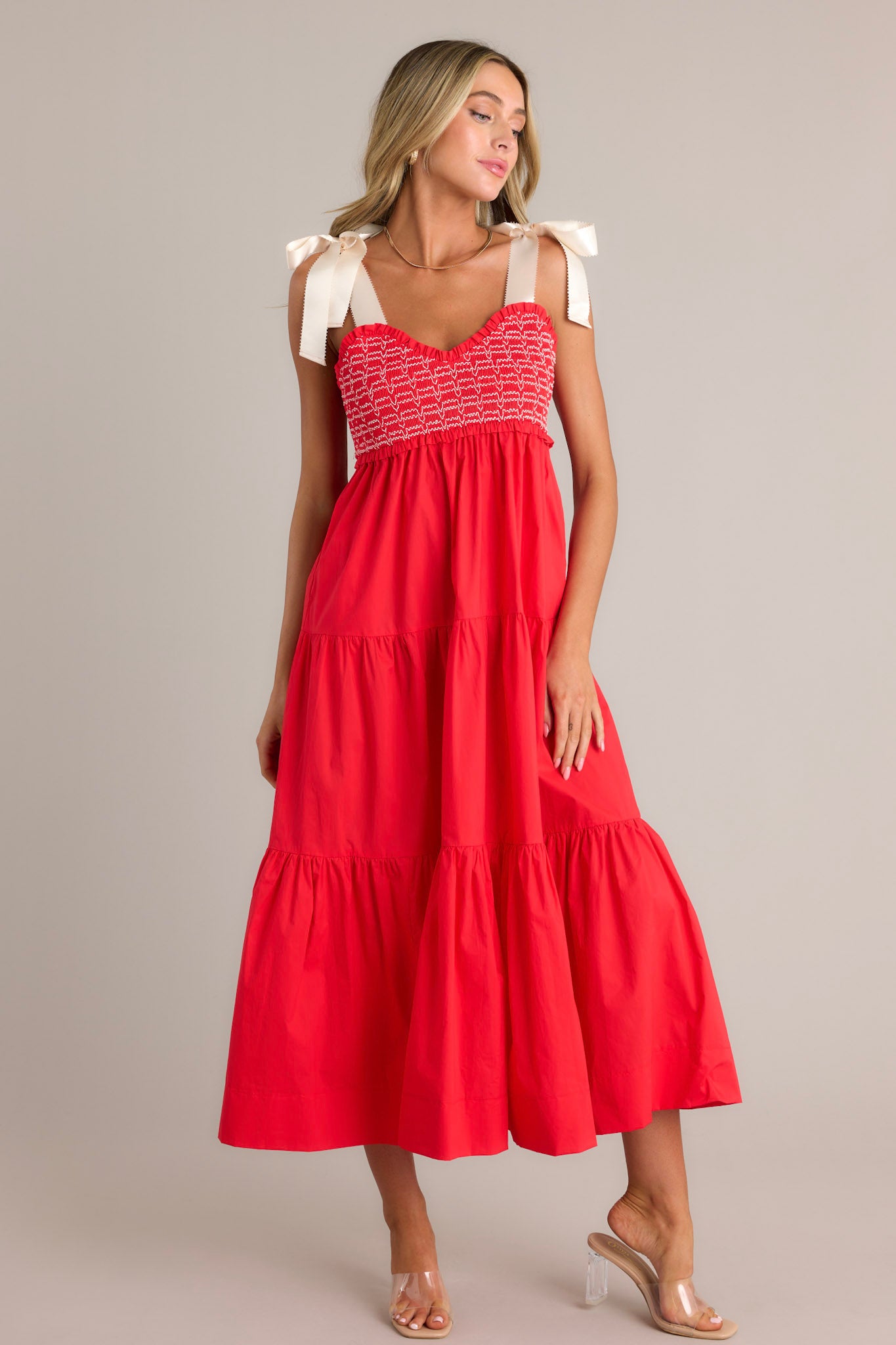 Front angled view of a red maxi dress featuring a v-neckline, thick self-tie straps, a fully smocked bodice, functional hip pockets, and a tiered design