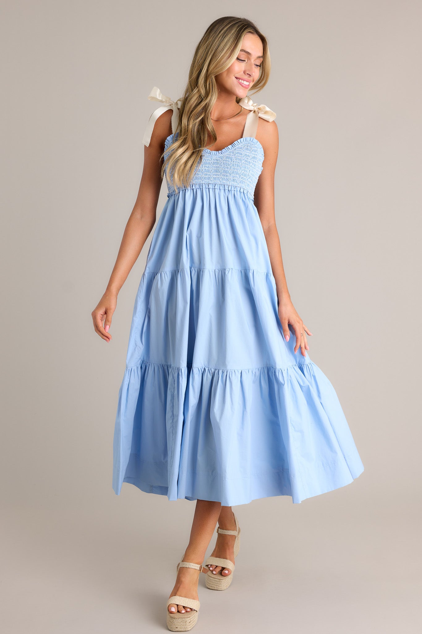 Action shot of a light blue maxi dress displaying the fit and movement, highlighting the v-neckline, thick self-tie straps, fully smocked bodice, functional hip pockets, and tiered design.