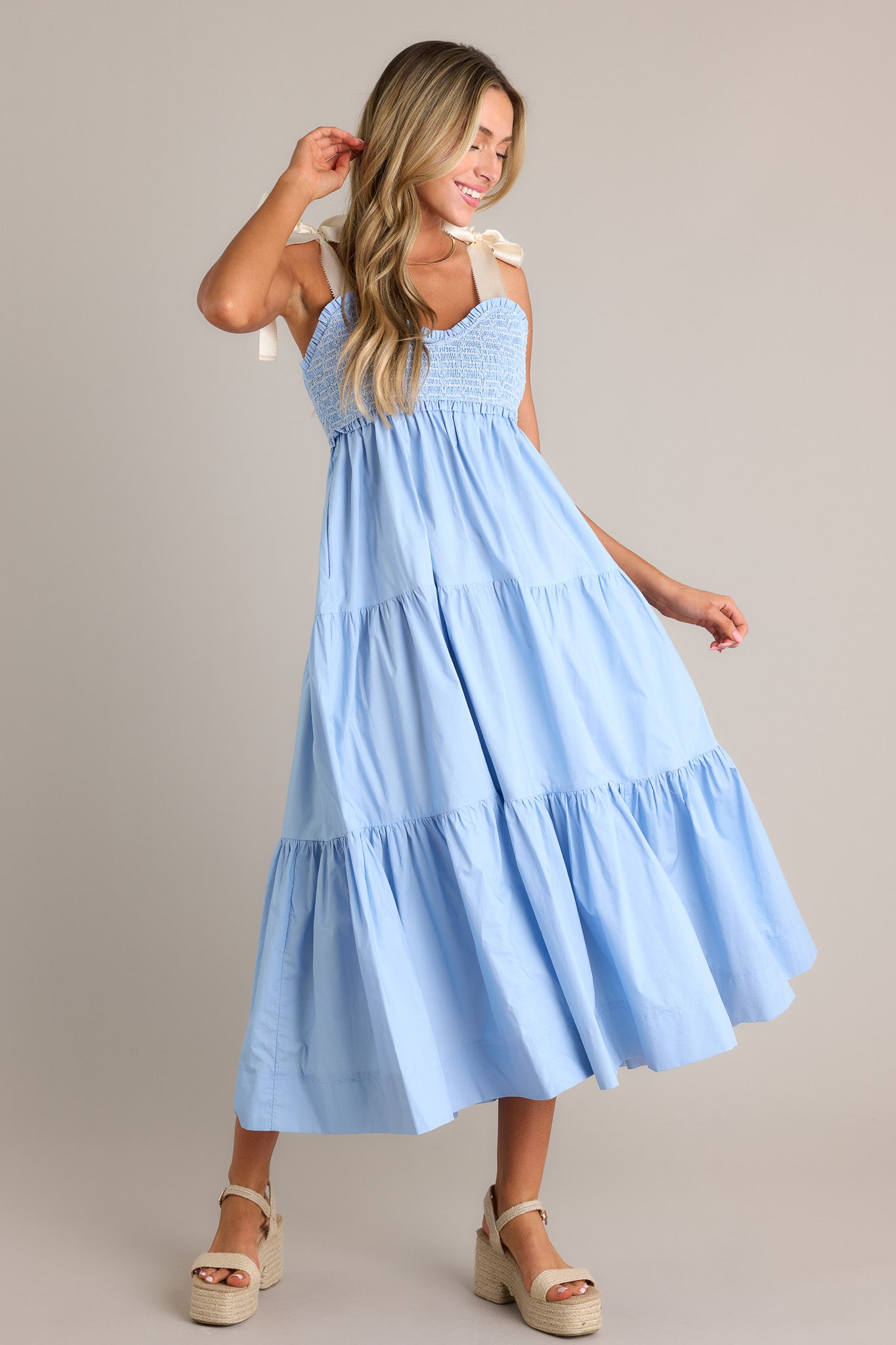 Side view of a light blue maxi dress showcasing the v-neckline, thick self-tie straps, fully smocked bodice, functional hip pockets, and tiered design.