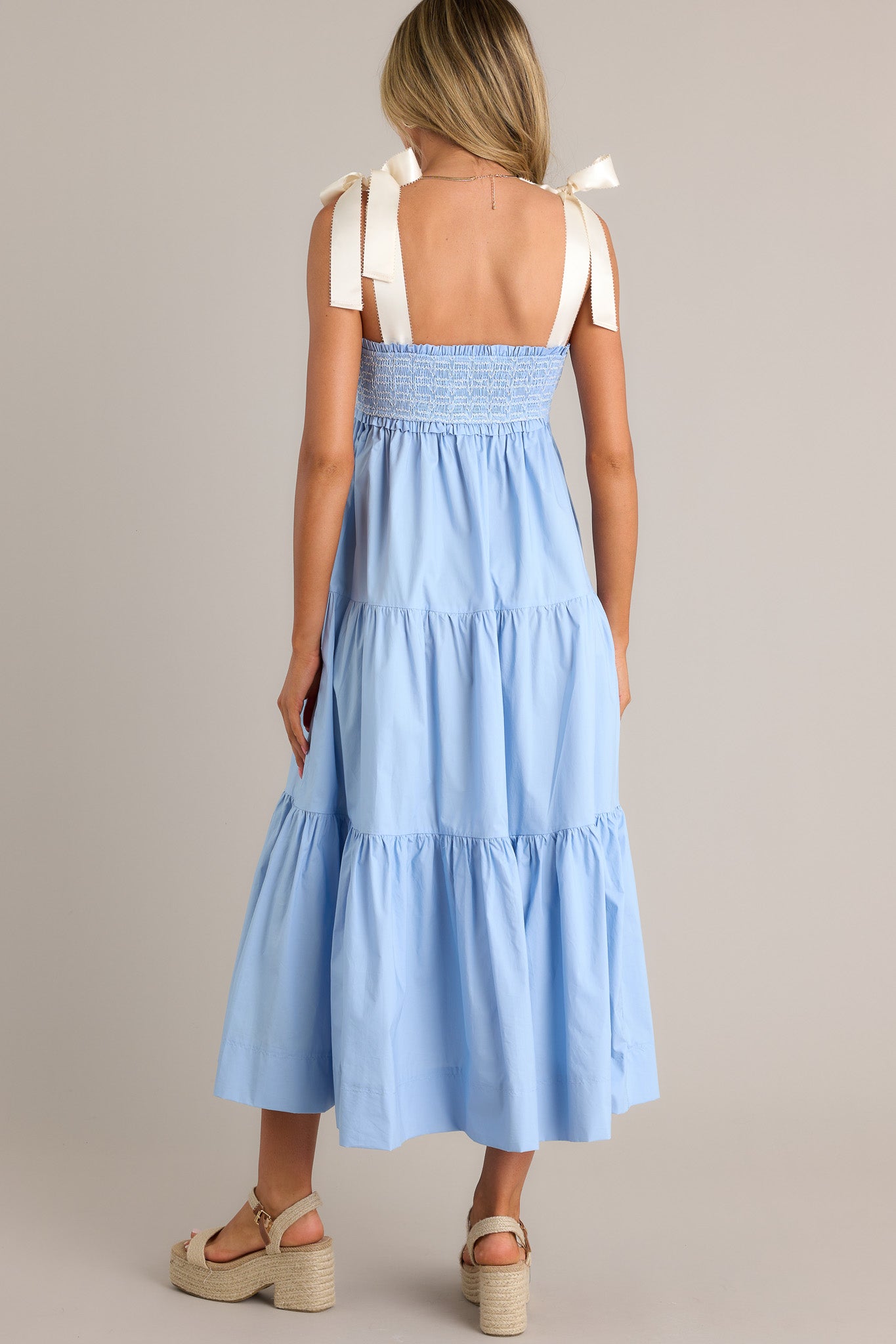 Back view of a light blue maxi dress highlighting the thick self-tie straps, fully smocked bodice, and tiered design.