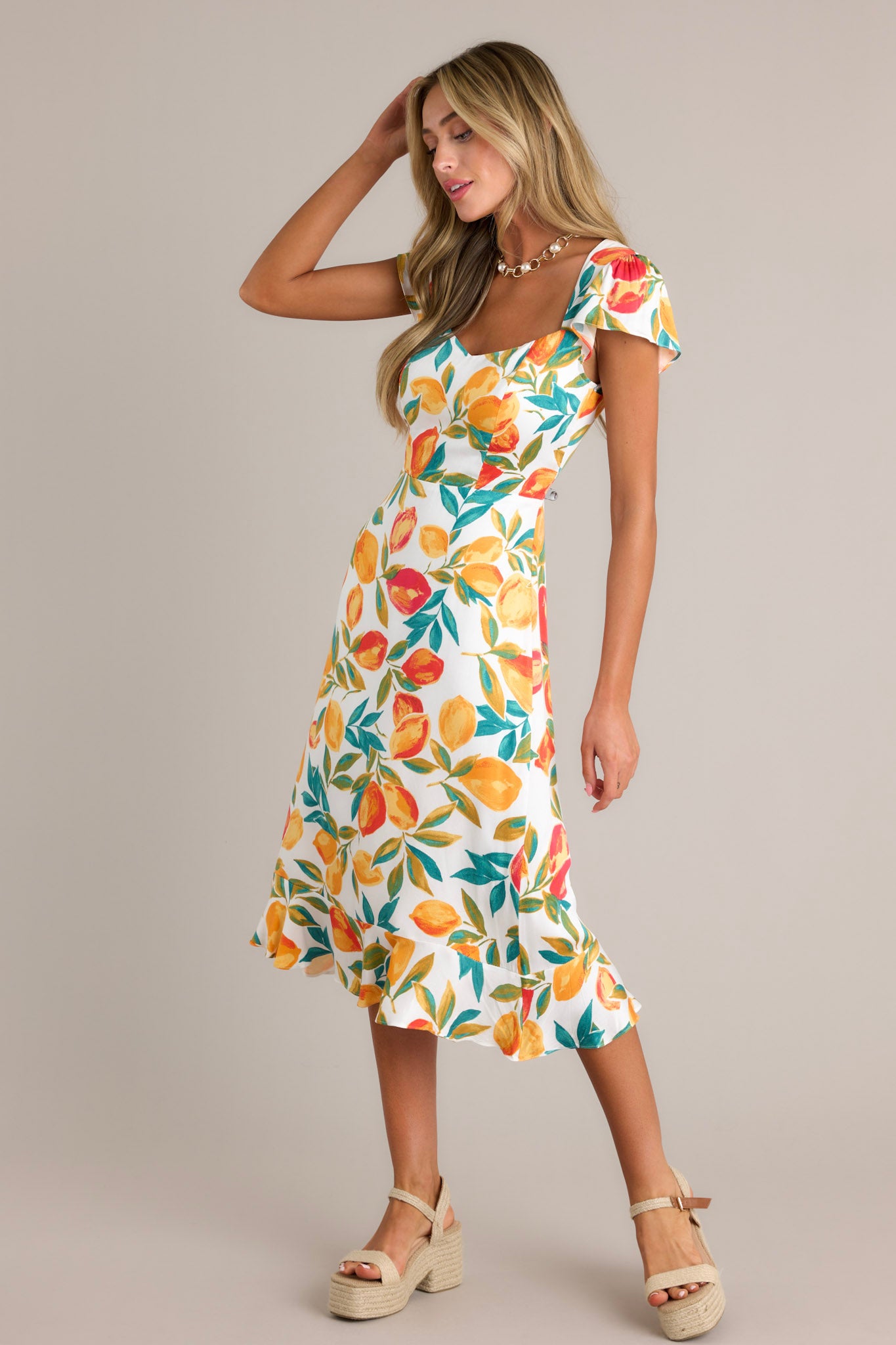 Side view of an ivory dress showcasing the v-neckline, citrus print, ruffled hemline, and short flutter sleeves.