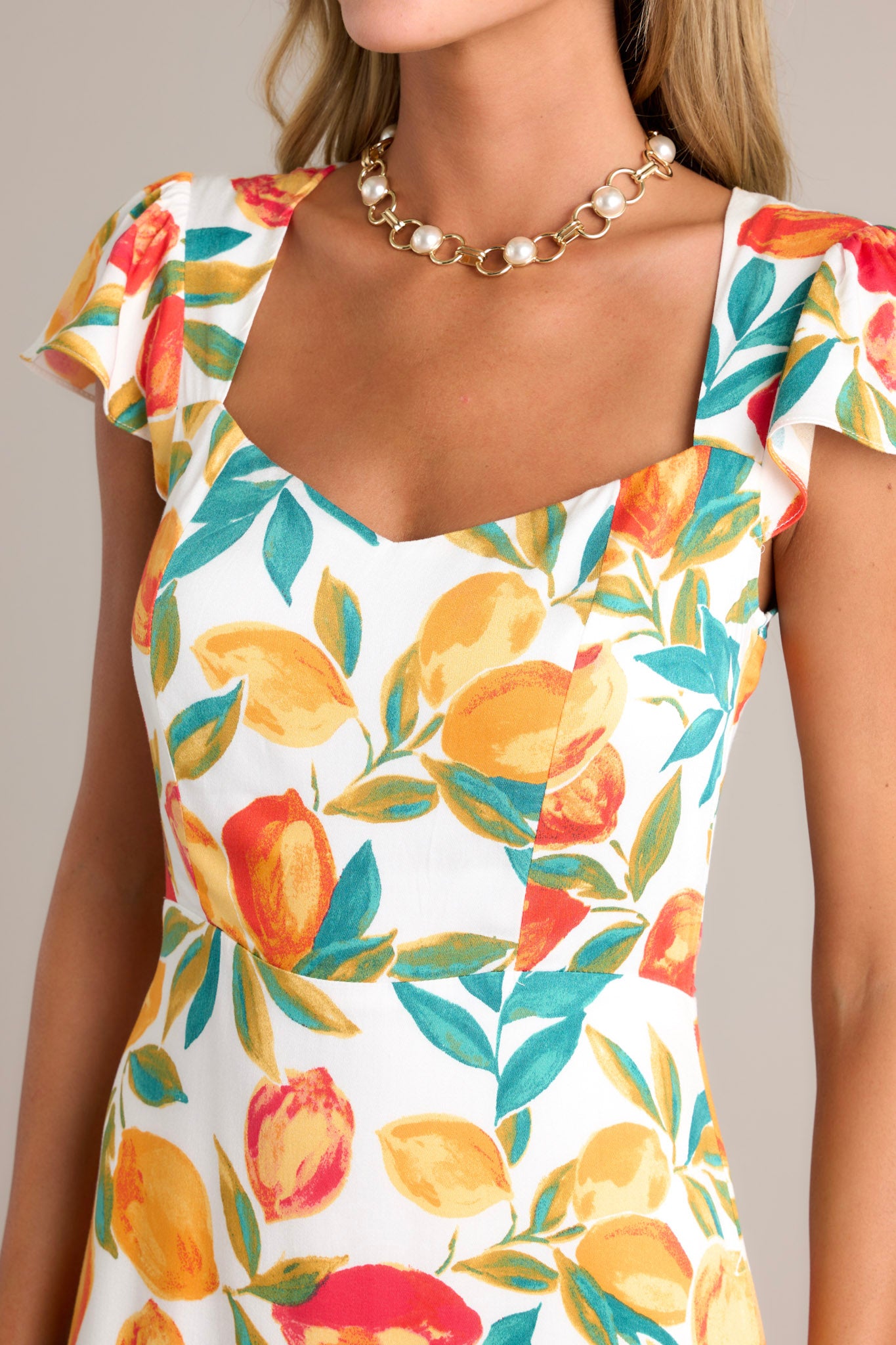 Close-up of the ivory dress showing the v-neckline, citrus print, and ruffled hemline.