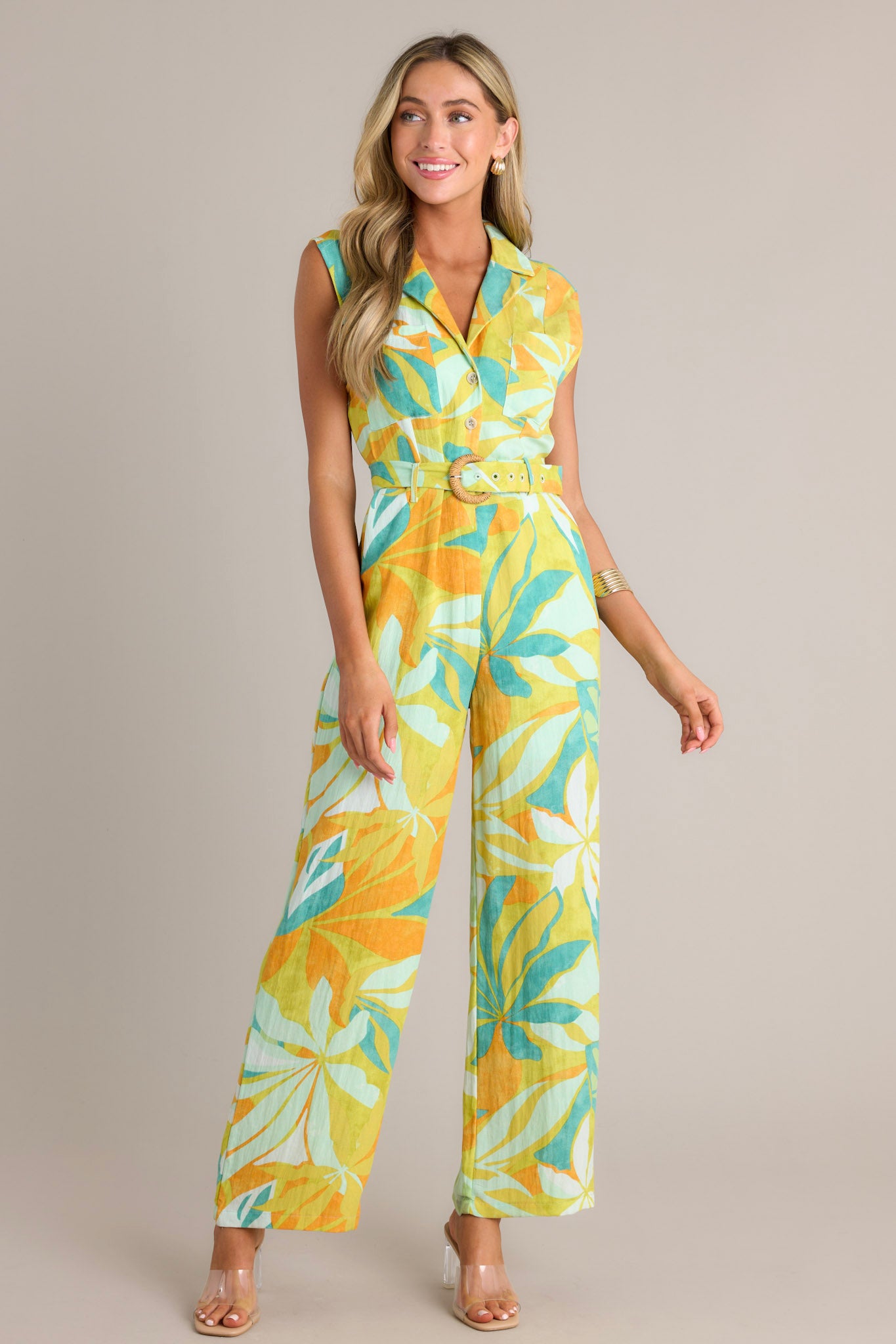 Front angled view of a lime green jumpsuit featuring a notched lapel collared v-neckline, breast pockets, functional buttons, an adjustable belt, belt loops, a functional zipper, functional hip pockets, and a wide leg design