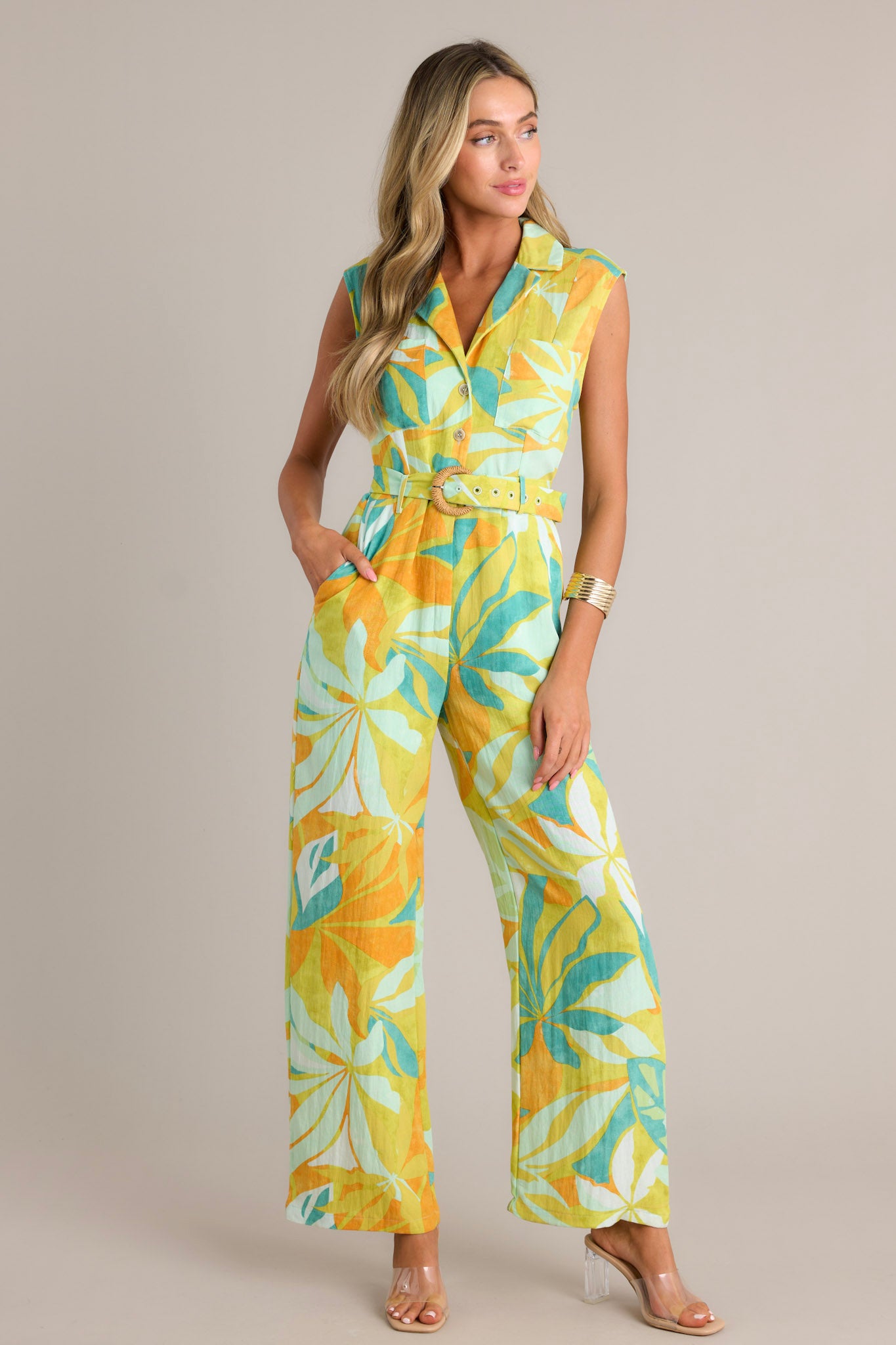 Full length view of a lime green jumpsuit with a notched lapel collared v-neckline, breast pockets, functional buttons, an adjustable belt, belt loops, a functional zipper, functional hip pockets, and a wide leg design