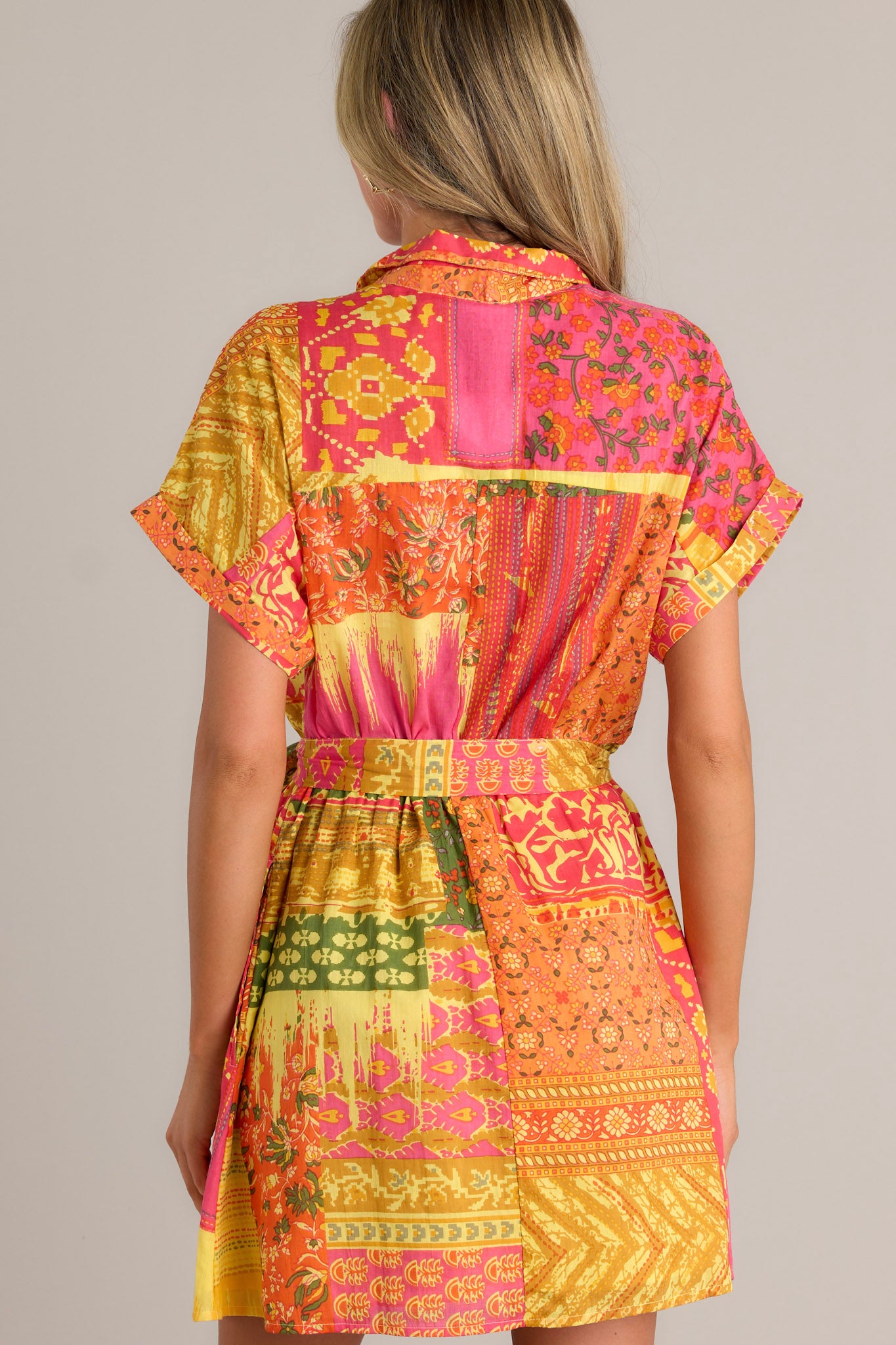 Back view of an orange mini dress highlighting the unique patchwork design, elastic waistband, self-tie waist belt, and overall fit.