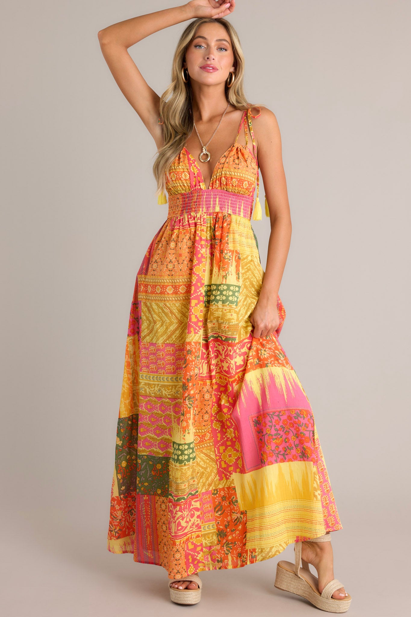 This orange maxi dress features a v-neckline, adjustable self-tie straps, a low back, a fully smocked waistband, a unique patchwork design, and a flowing silhouette.