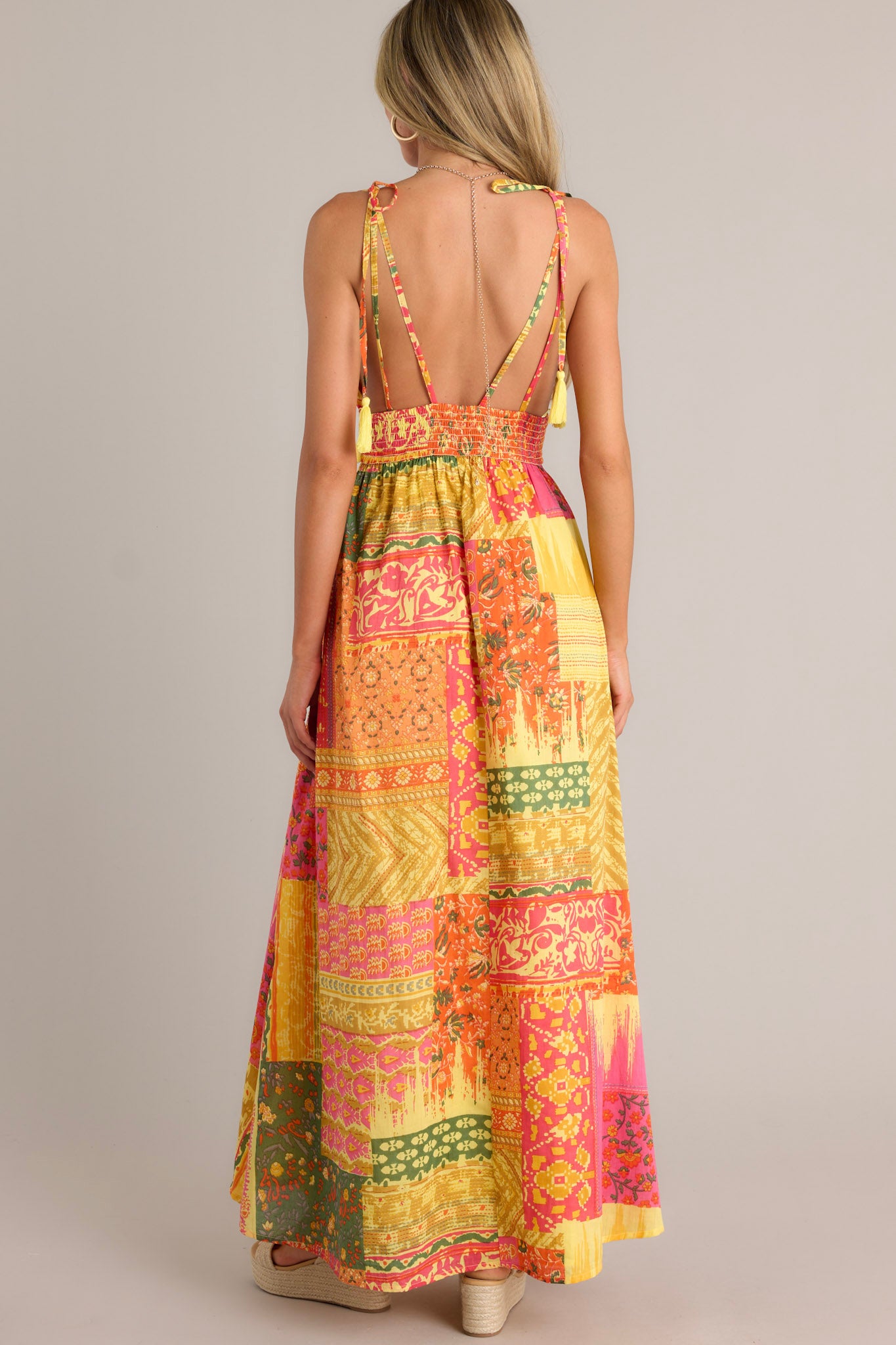 Back view of an orange maxi dress highlighting the low back, adjustable self-tie straps, fully smocked waistband, and overall fit.