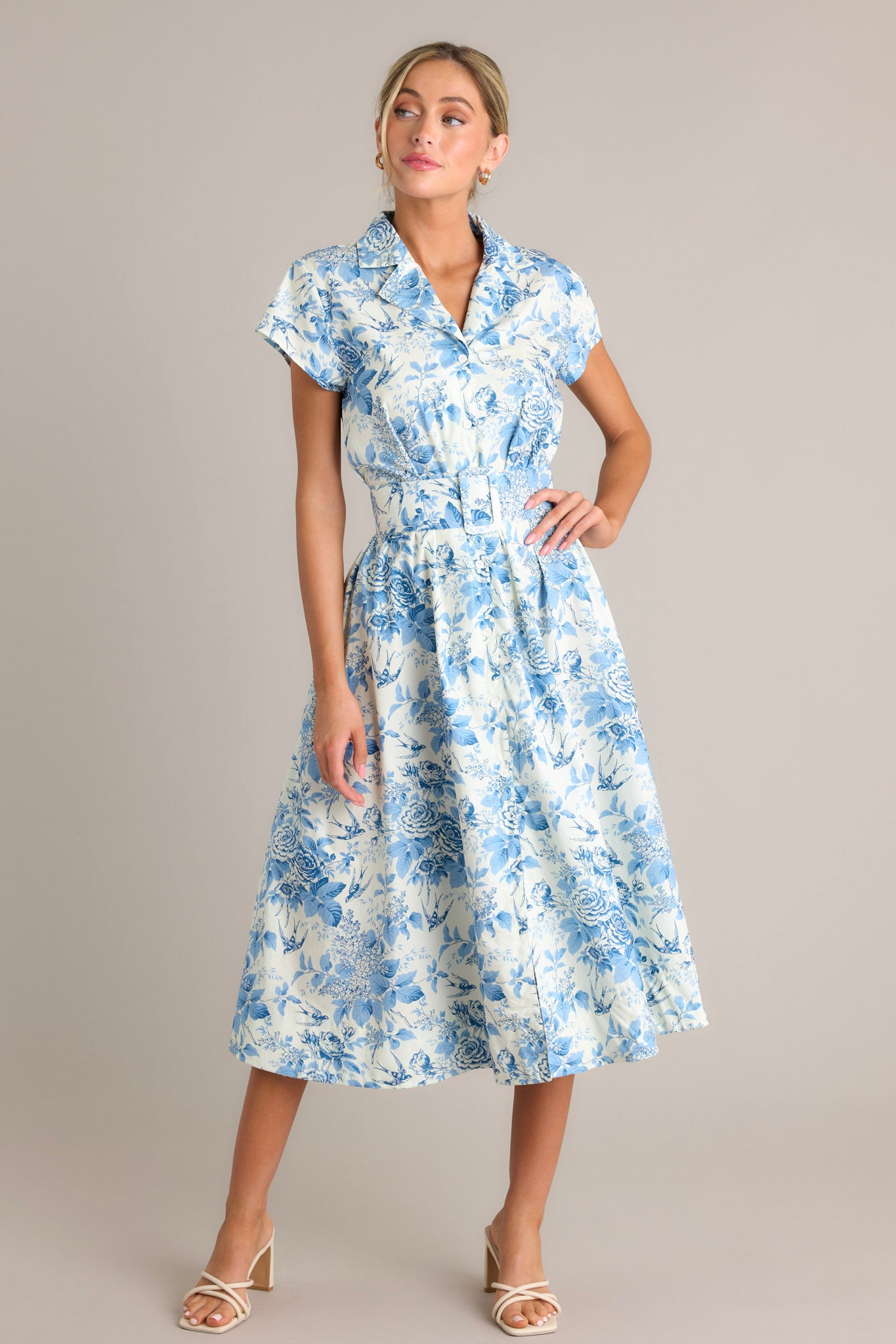 Front angled view of a dress featuring a notched lapel collared v-neckline, a full button front, belt loops, a functional belt, functional hip pockets, and a front slit