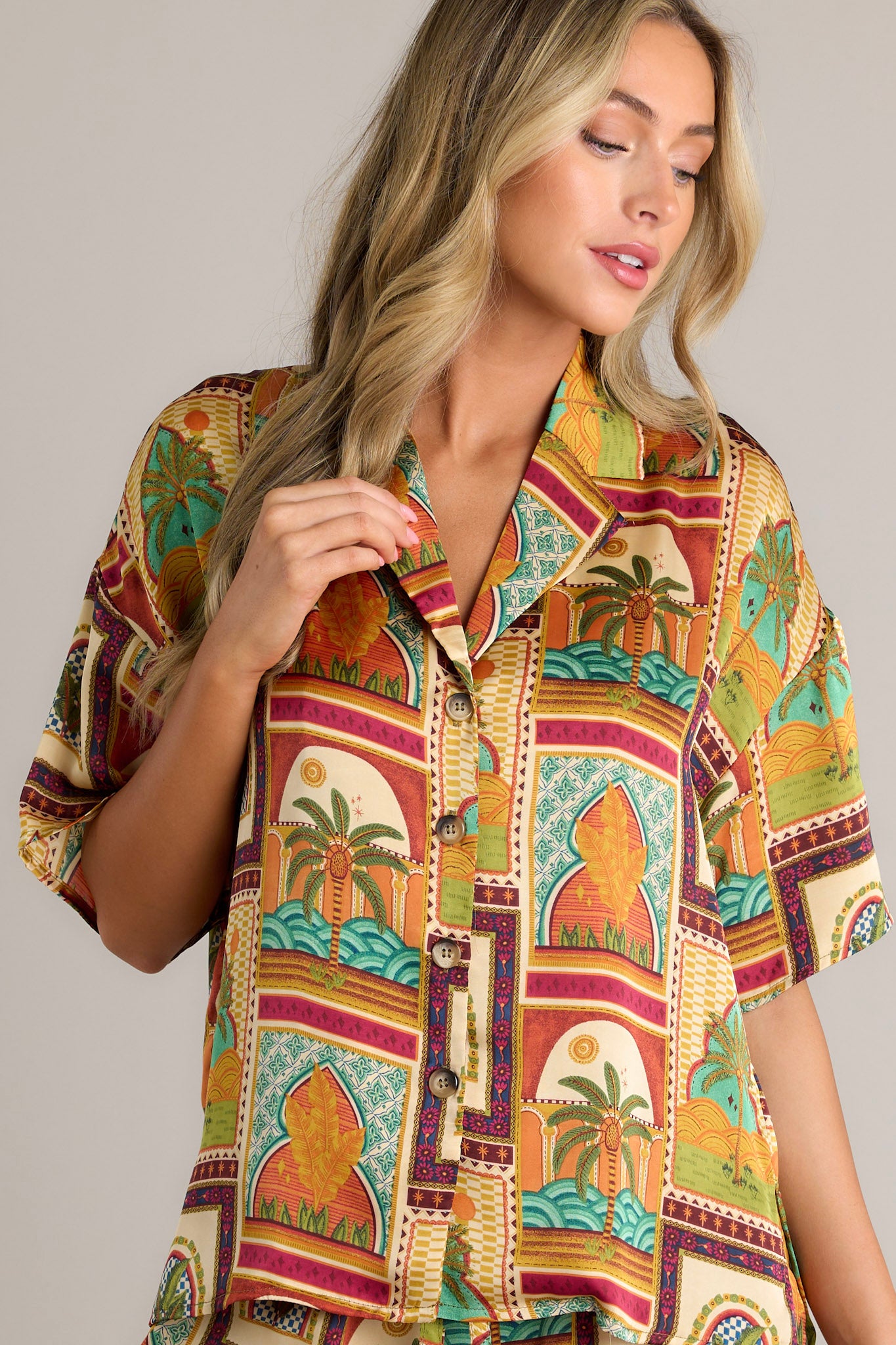 Front angled view of a mustard top featuring a notched lapel collared neckline, functional buttons down the front, lightweight fabric, a unique print, and a split hemline